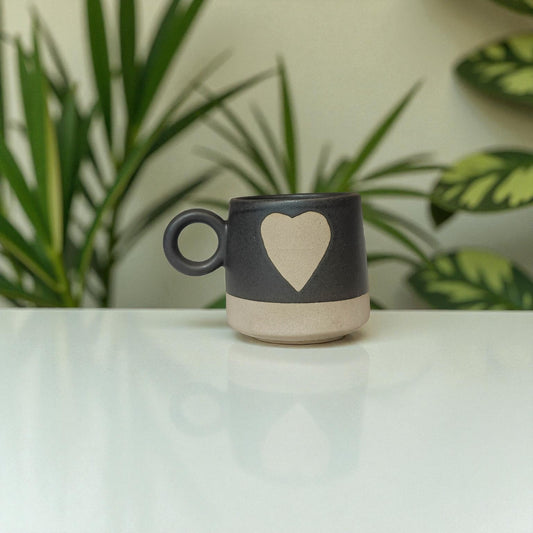 Ceramic mug with a heart design on a white surface with plants in the background