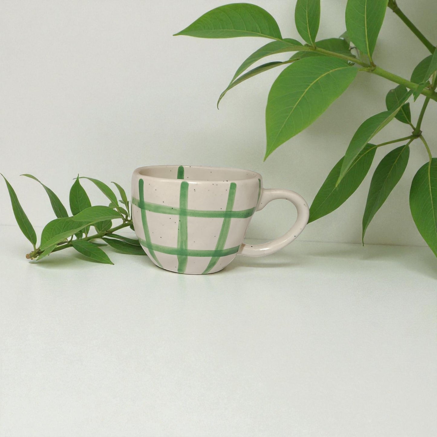 Ceramic mug with green checkered pattern on a white surface with green leaves.