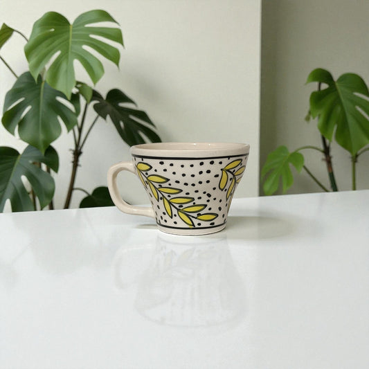Ceramic mug with leaf pattern on a white surface with plants in the background