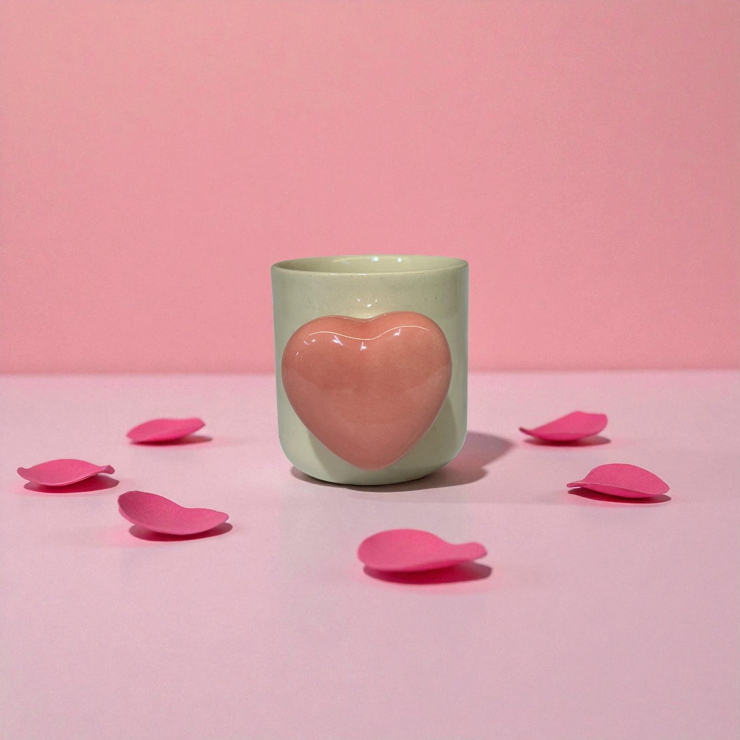 Mint green mug with a pink heart-shaped handle on a pink background with scattered pink petals.