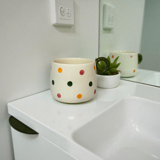 Polka dot mug on a bathroom counter with a plant and mirror reflection.