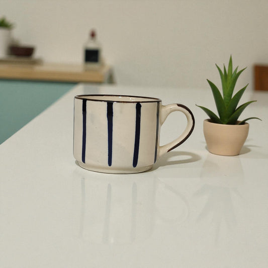 White mug with black stripes on a white surface next to a plant