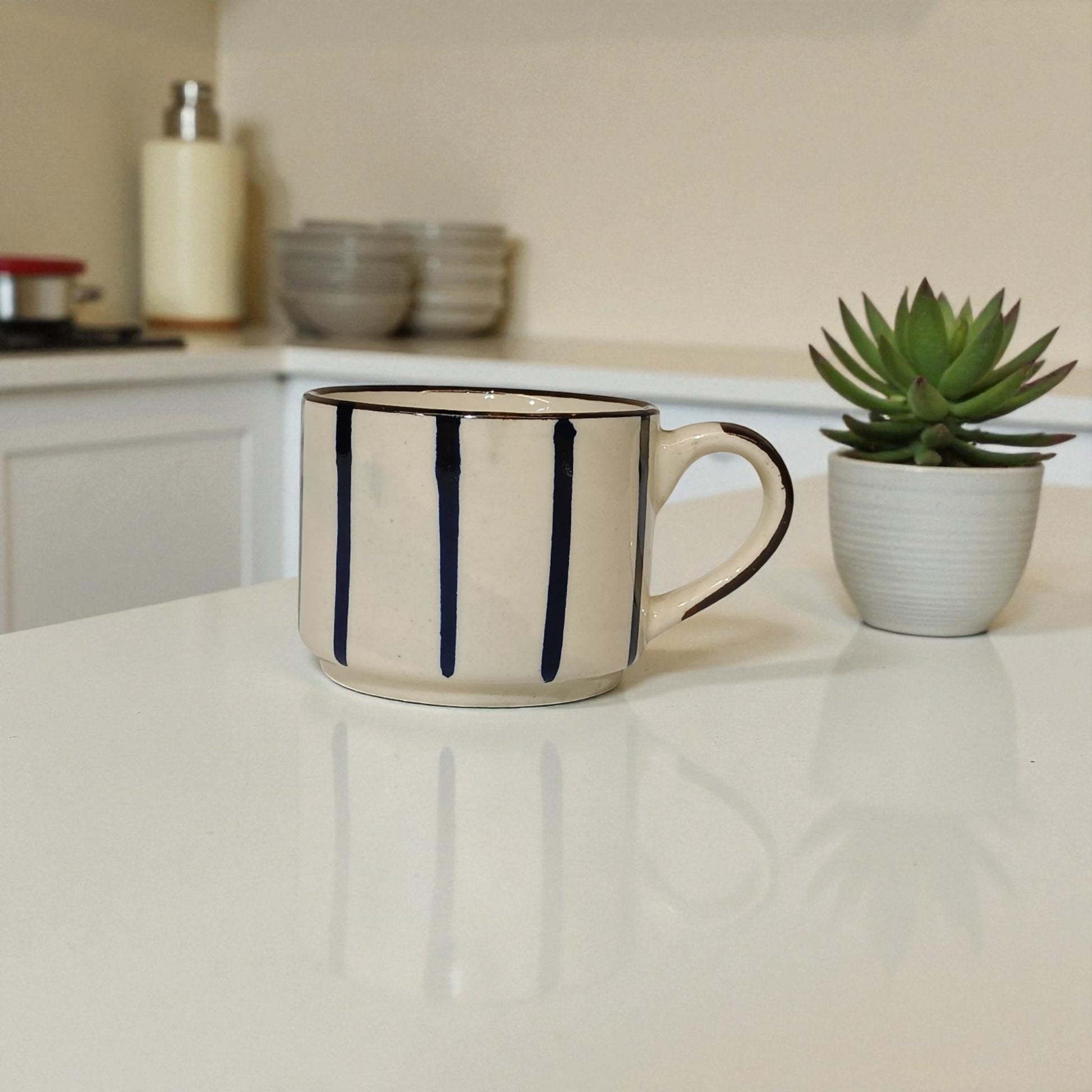 Beige mug with black stripes on a kitchen counter with a potted plant in the background.
