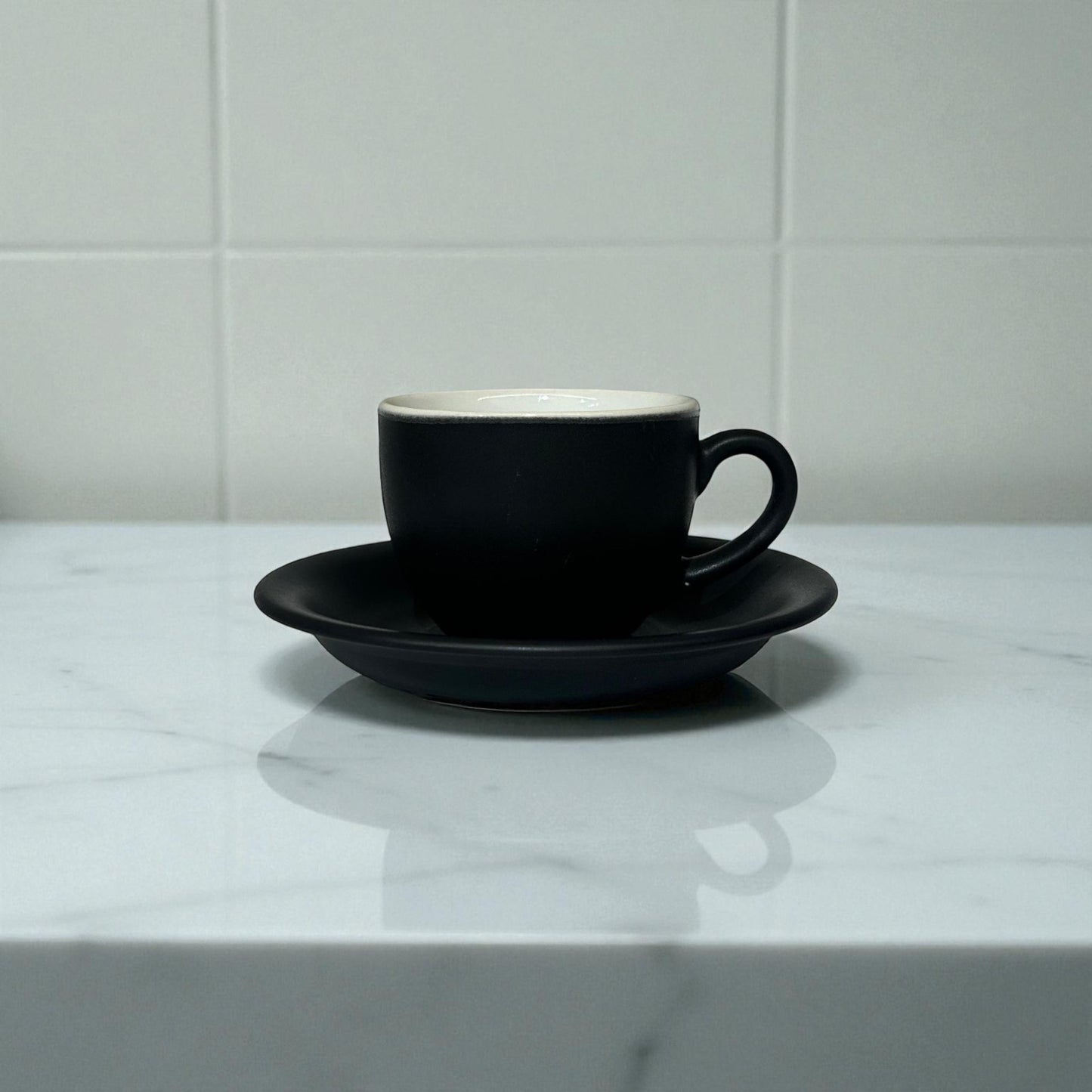 Black coffee cup and saucer on a marble surface with a white tiled wall background