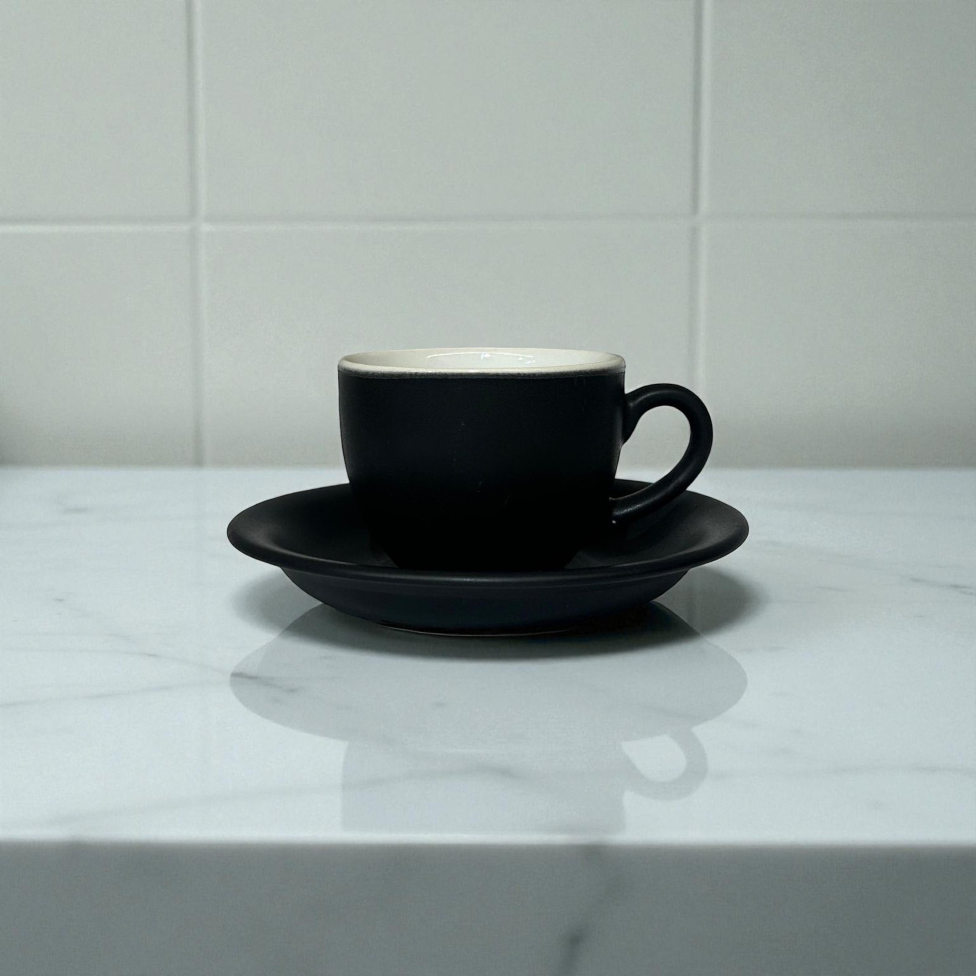Black coffee cup and saucer on a marble surface with a white tiled wall background