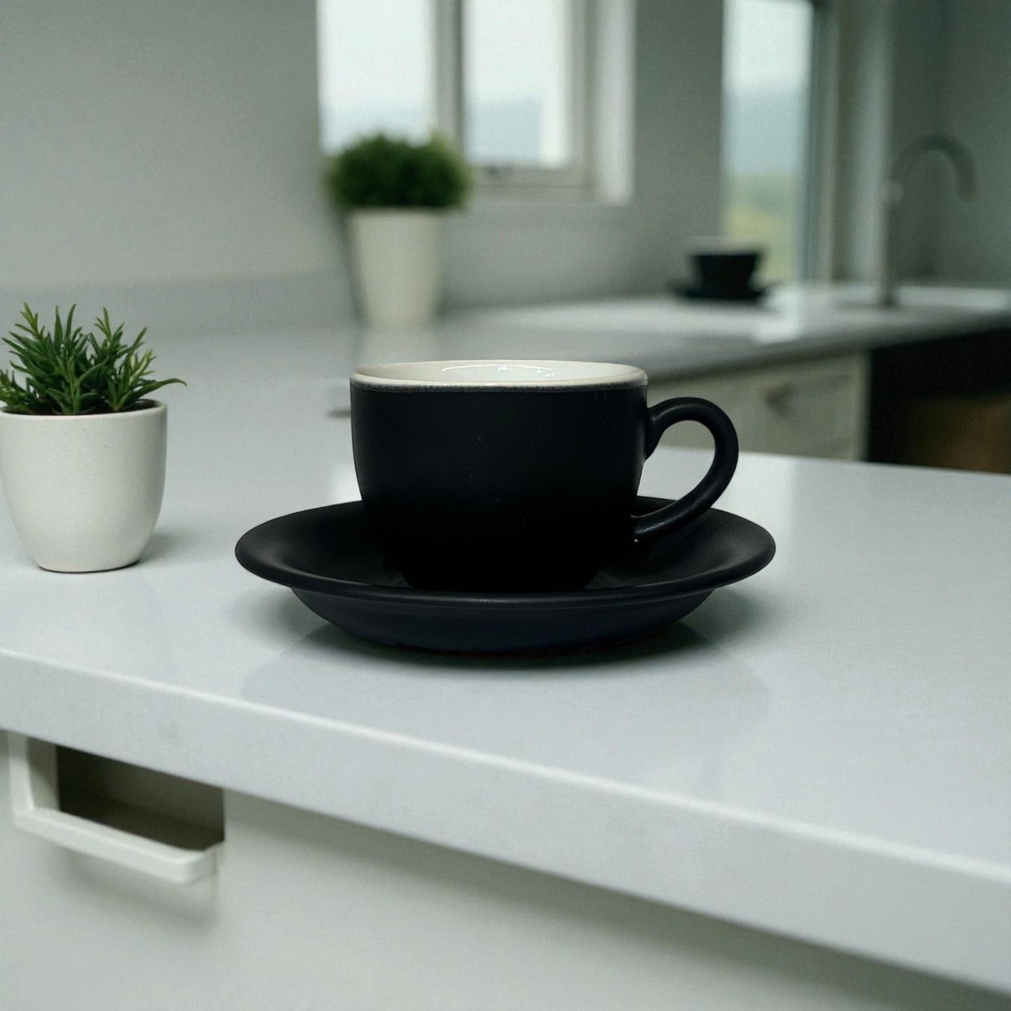 Black cup and saucer on a white countertop with a blurred kitchen background
