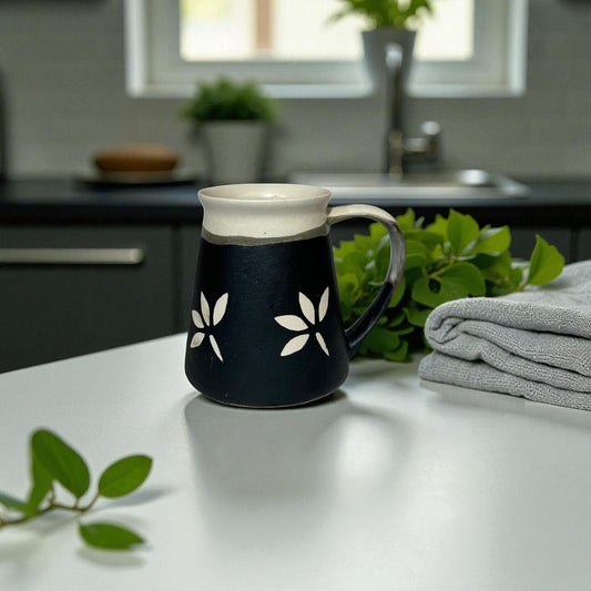 Black mug with white floral designs on a kitchen counter with plants and a towel.