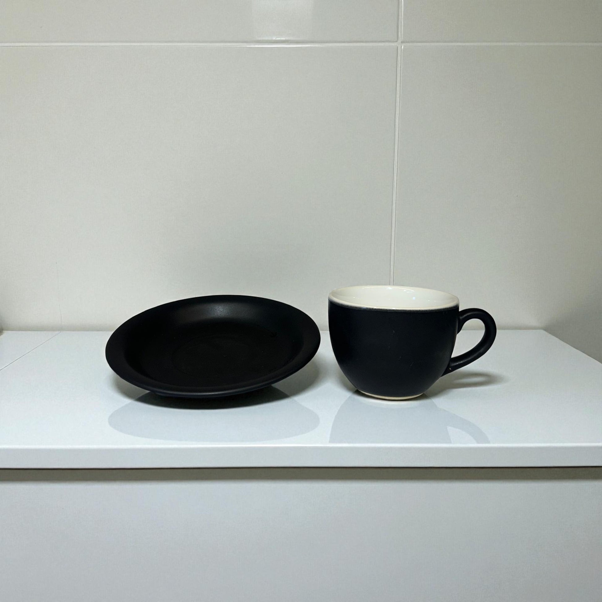 Black plate and mug on a white countertop with a tiled wall background