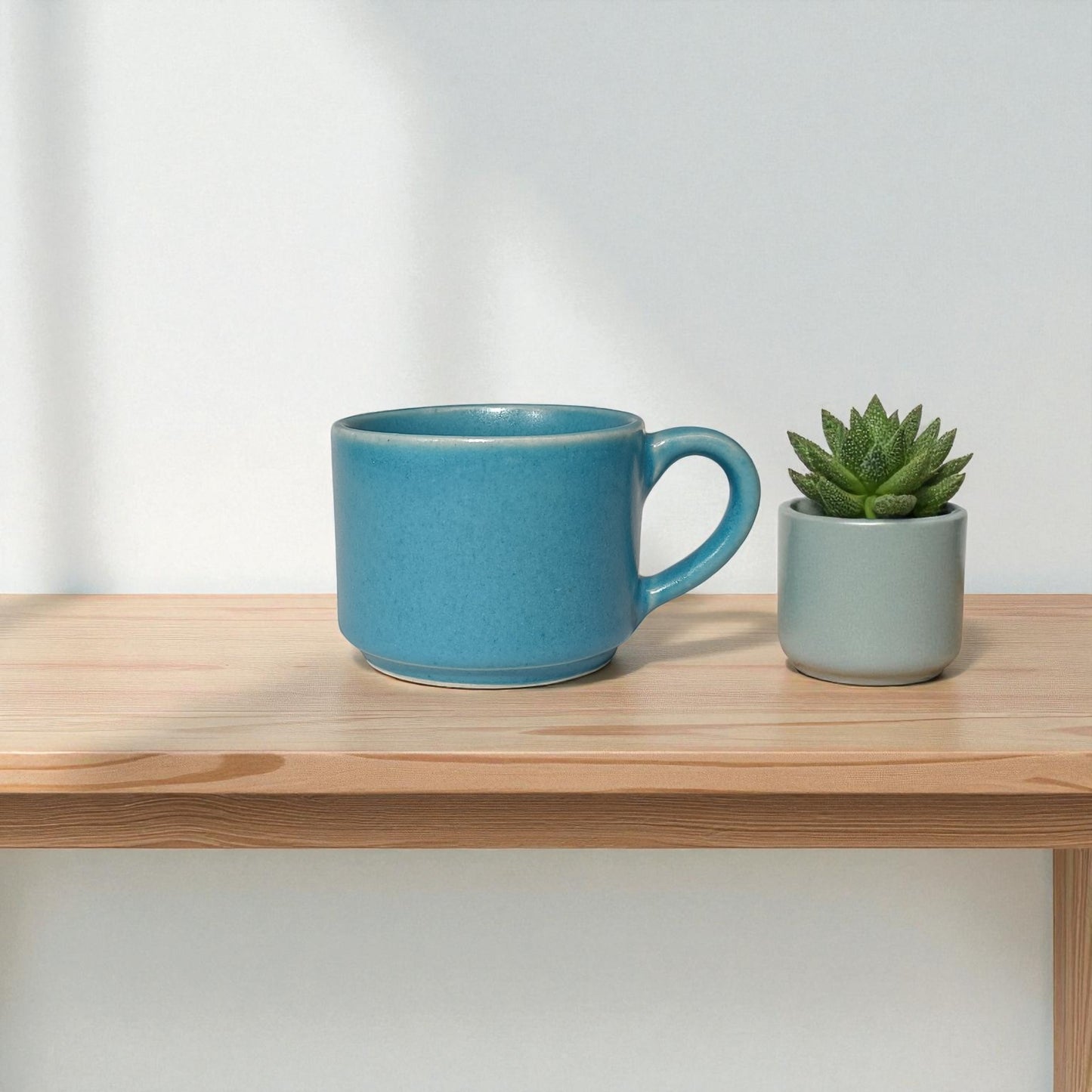 Blue mug and small potted plant on a wooden shelf with a light gray background