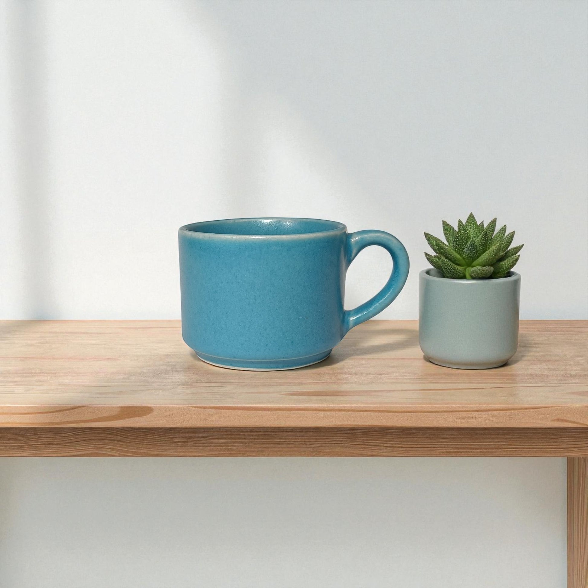 Blue mug and small potted plant on a wooden shelf with a light gray background