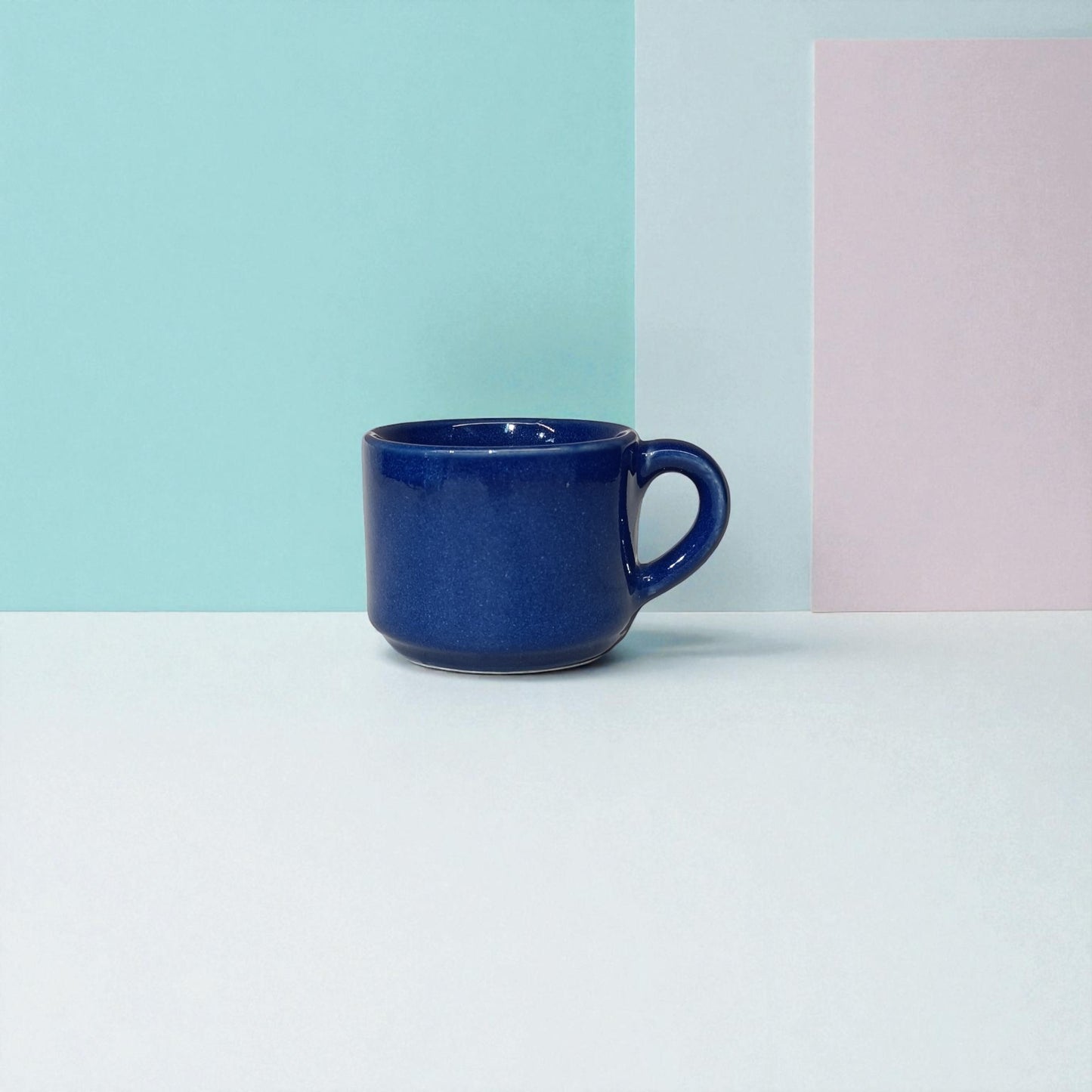 Blue mug on a white surface with a light blue and pink geometric background