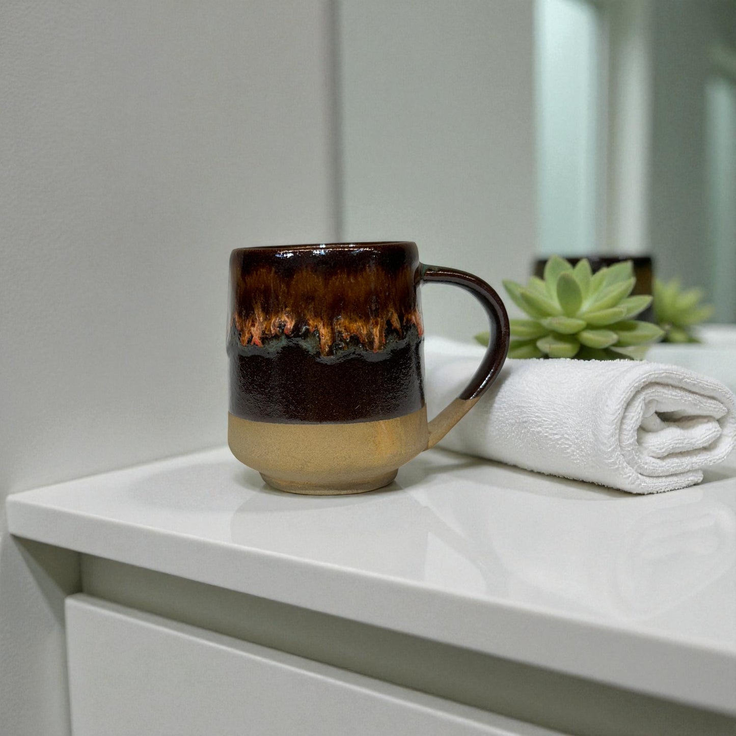 Brown ceramic mug on a white surface with a towel and plant in the background