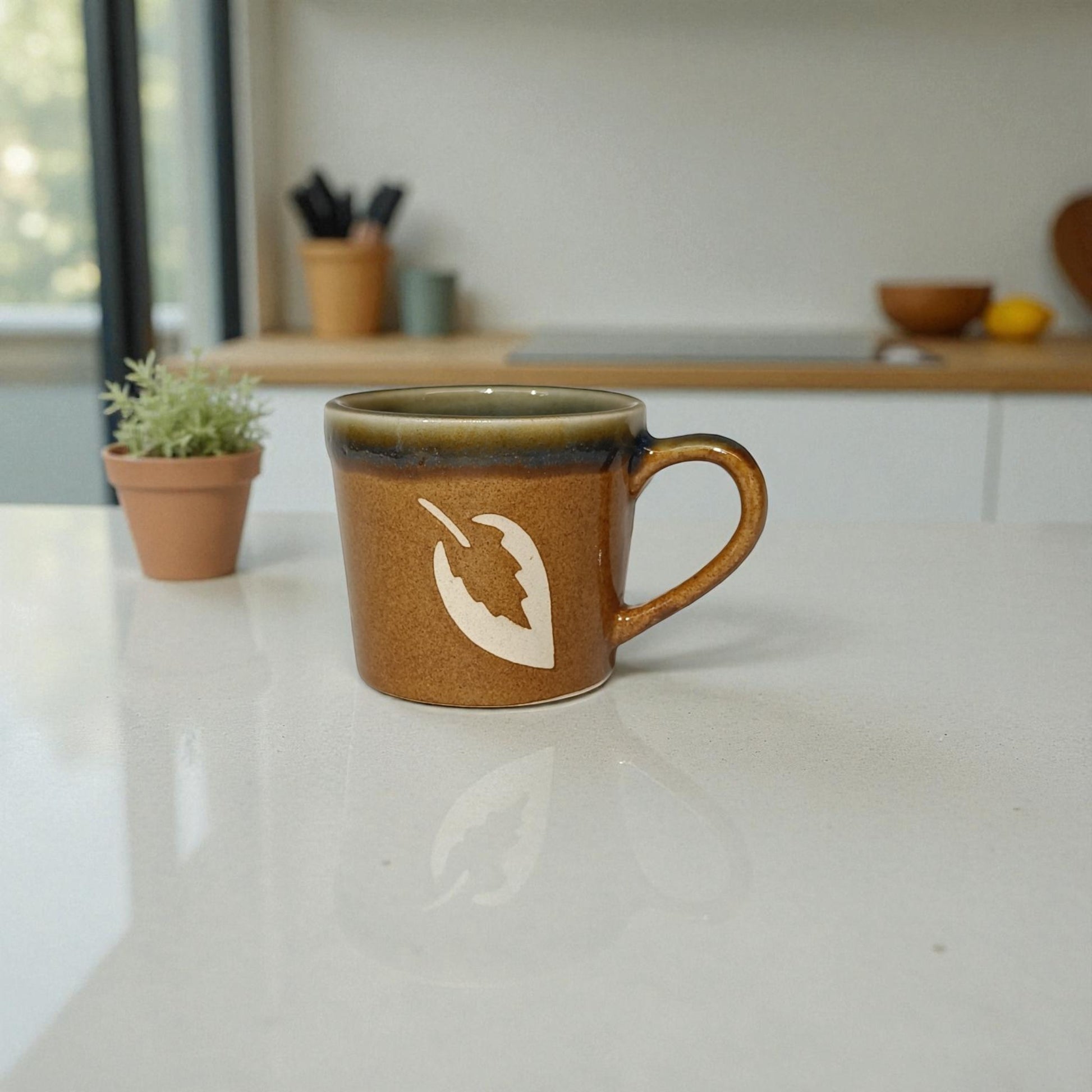 Brown ceramic mug with a white design on a white surface, with a blurred kitchen background.