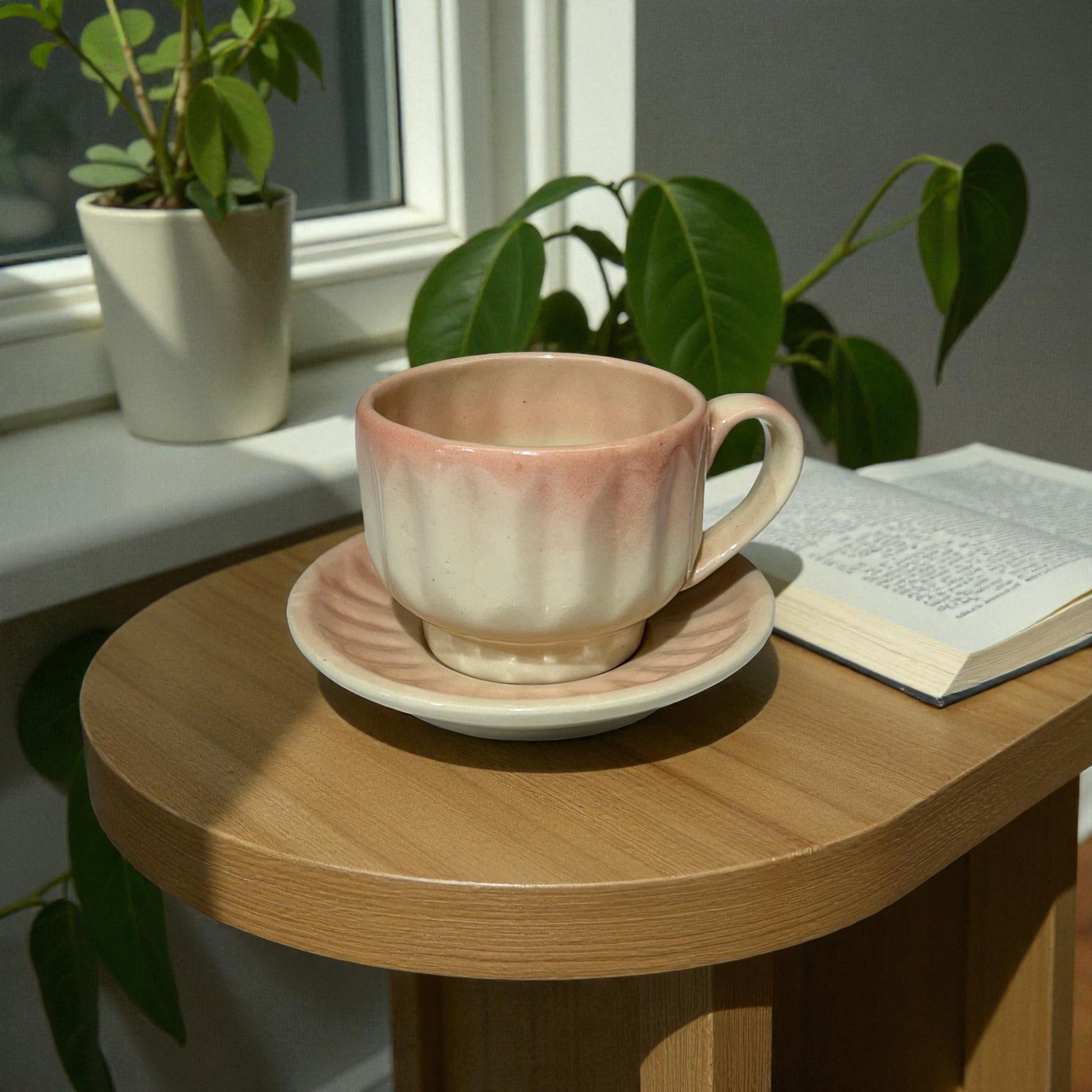 Ceramic cup and saucer on a wooden table with plants and a book in the background