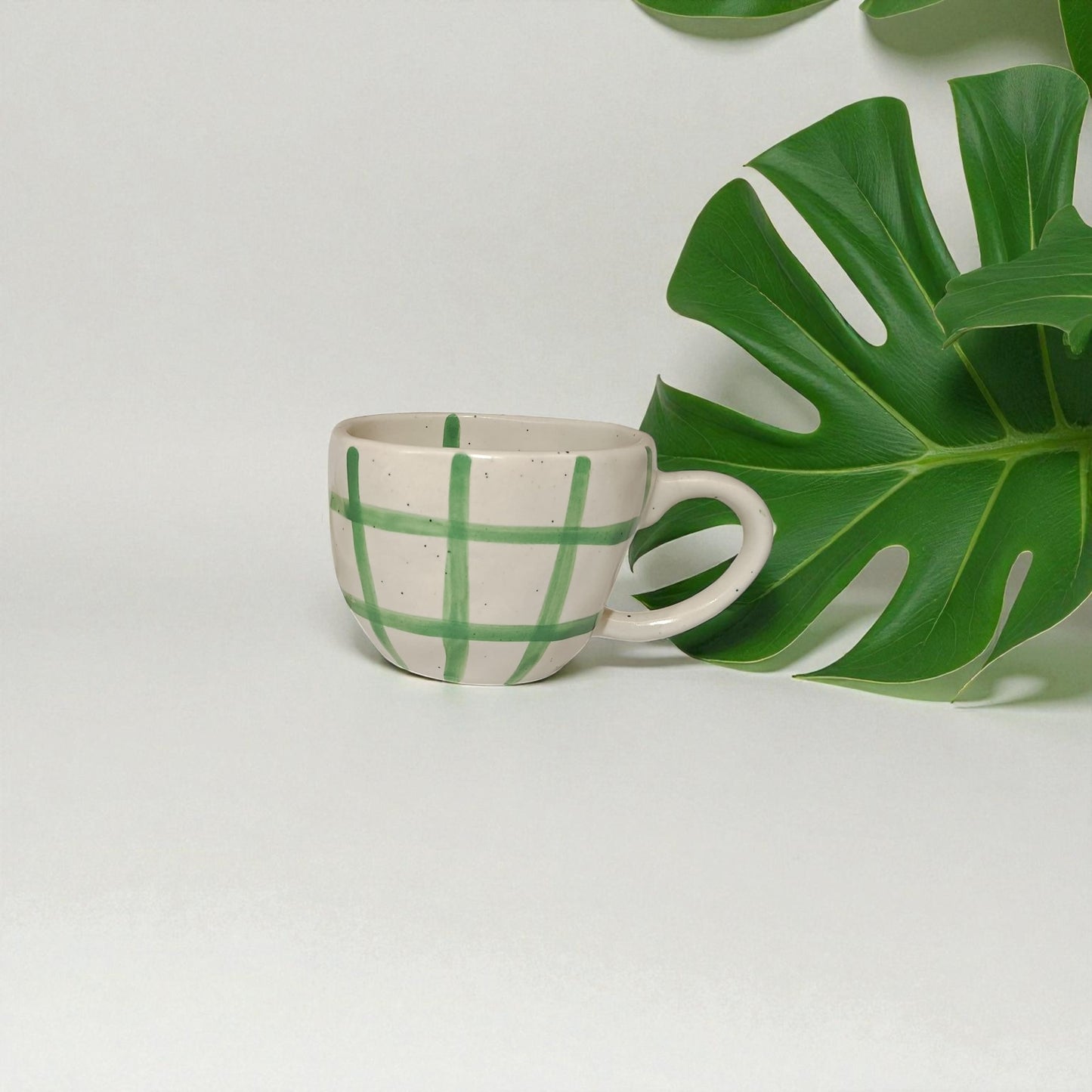 Ceramic cup with green leaf pattern next to a large green leaf on a light gray background