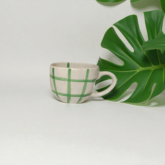 Ceramic cup with green leaf pattern next to a large green leaf on a light gray background