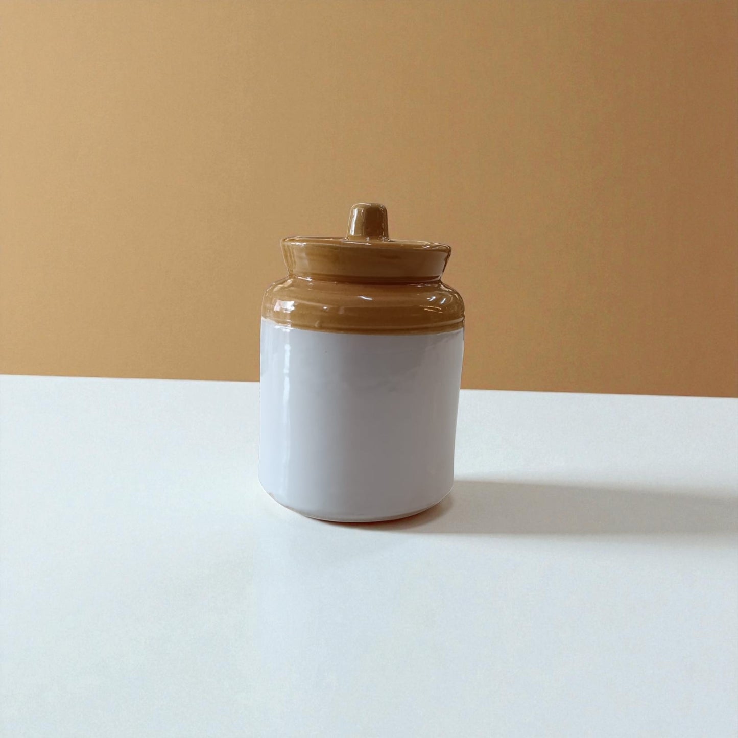 Ceramic jar with a brown lid on a white surface against a beige background