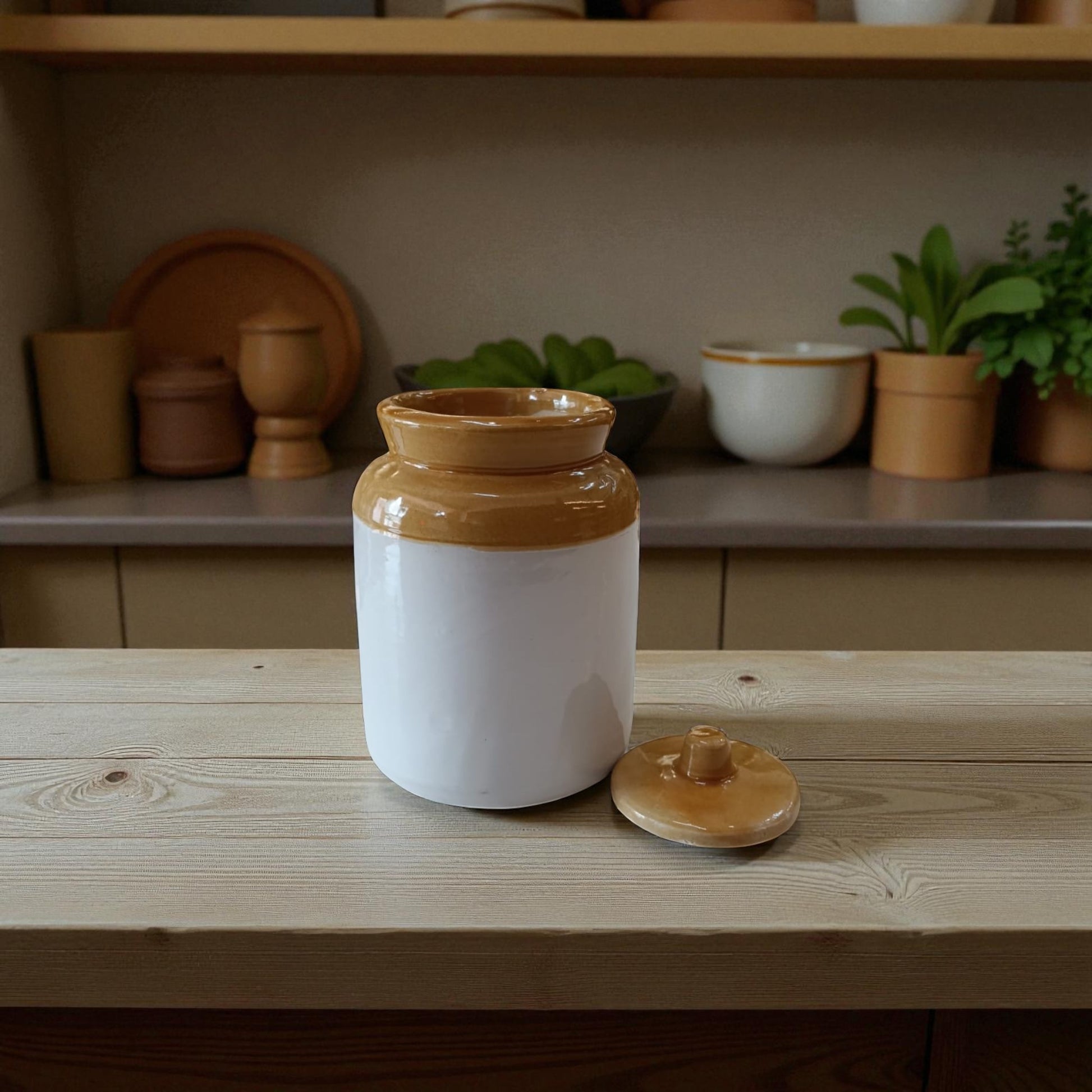 Ceramic jar with a brown lid on a wooden surface, with a shelf of kitchen items in the background.