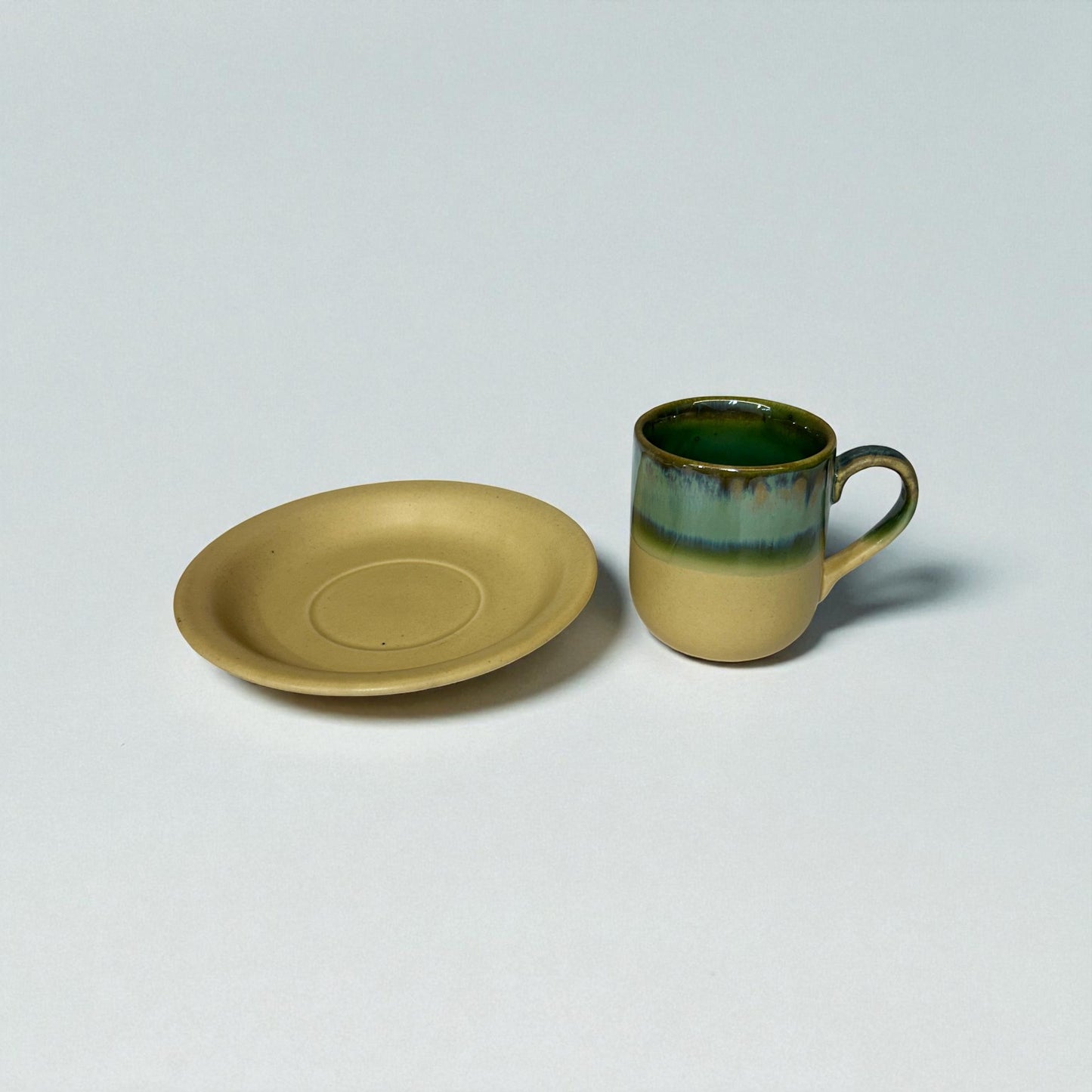 Ceramic mug and plate with green interior on a light gray background