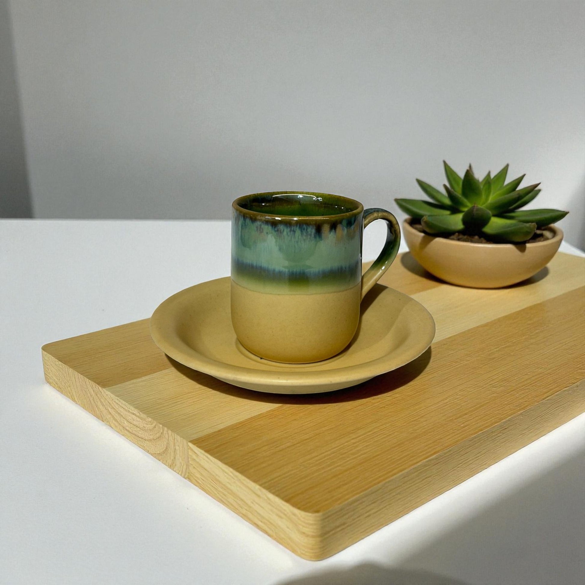 Ceramic mug and saucer with a small potted plant on a wooden tray