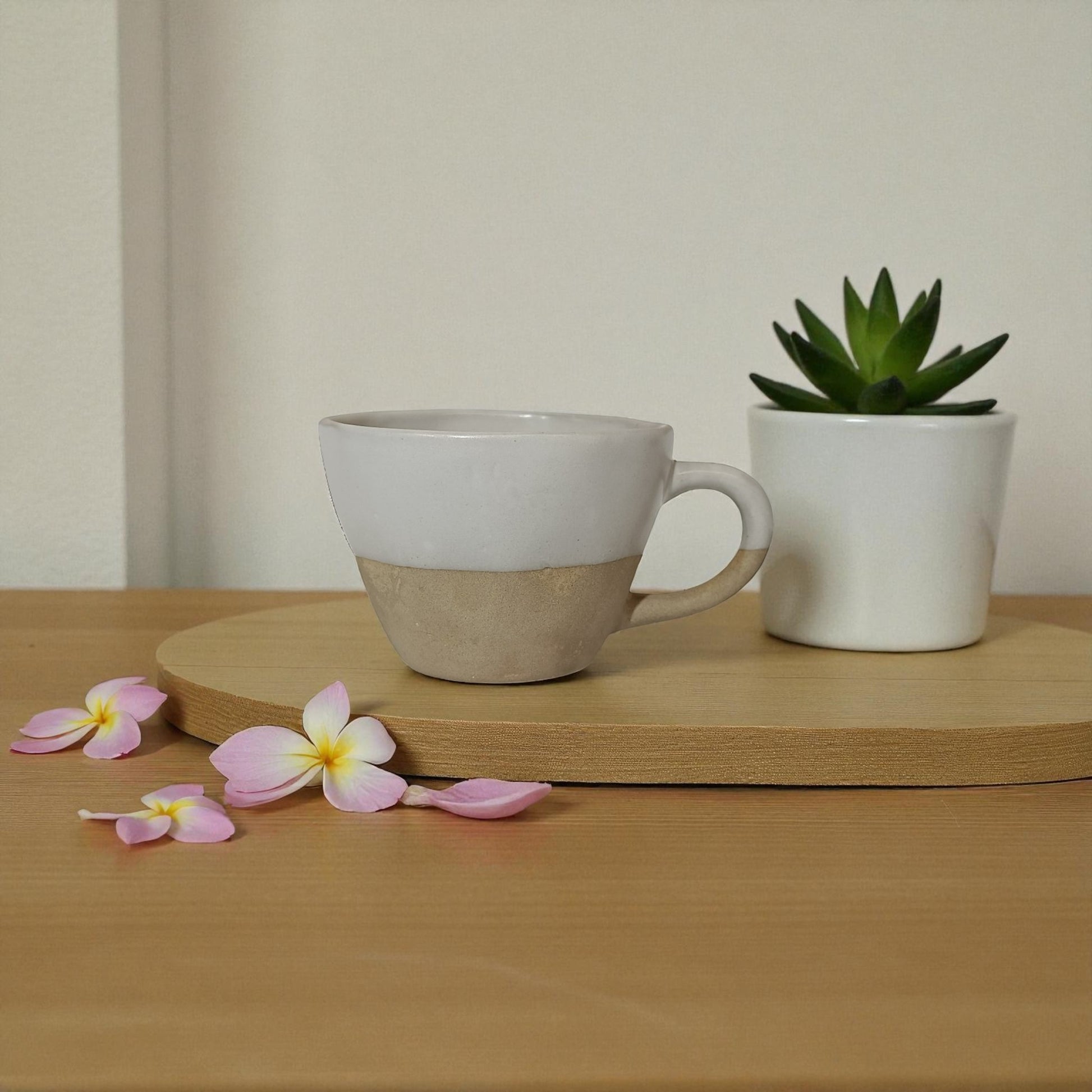 Ceramic mug and small plant on a wooden surface with pink flowers.