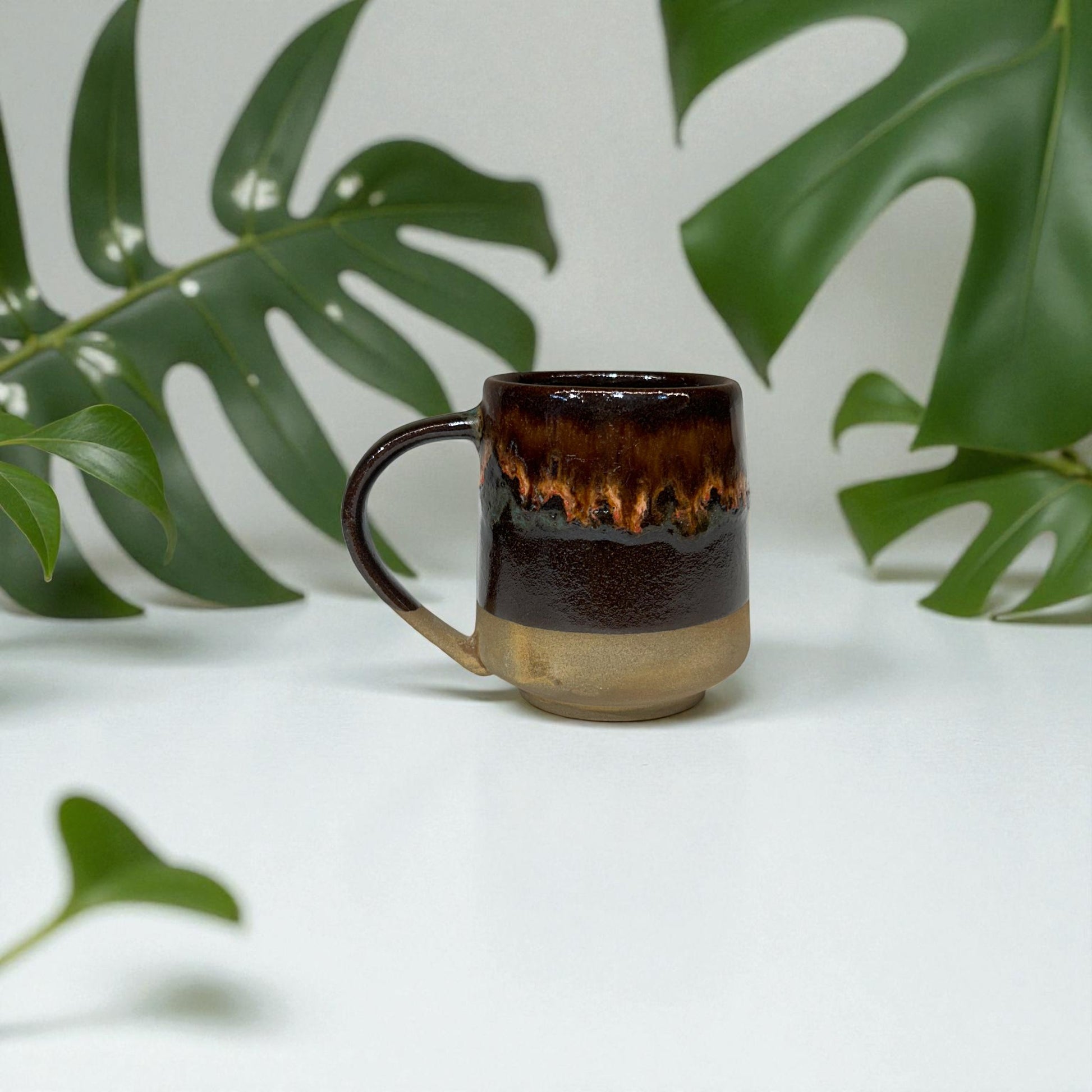 Ceramic mug with a gradient finish in front of green leaves on a white background