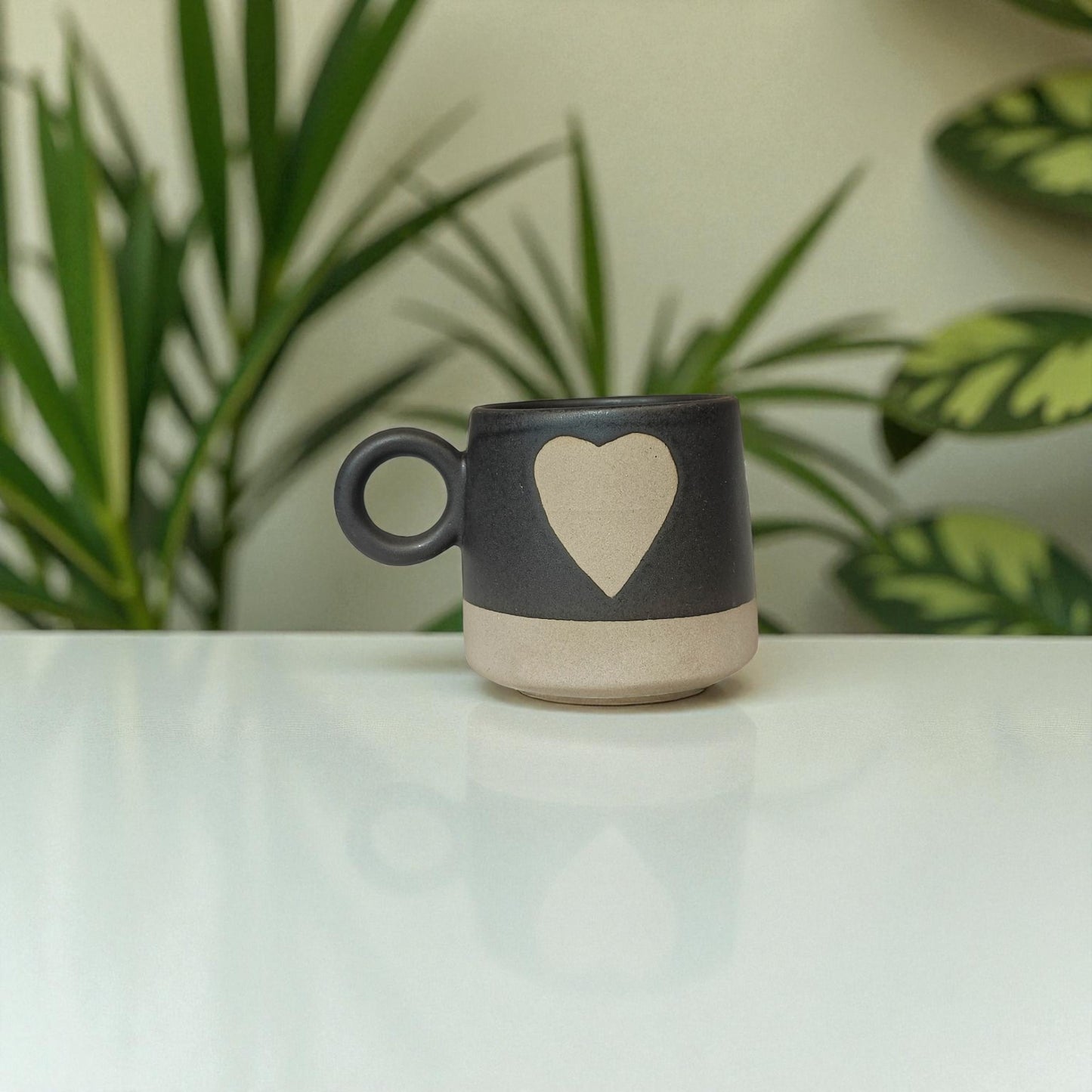 Ceramic mug with a heart design on a white surface with plants in the background