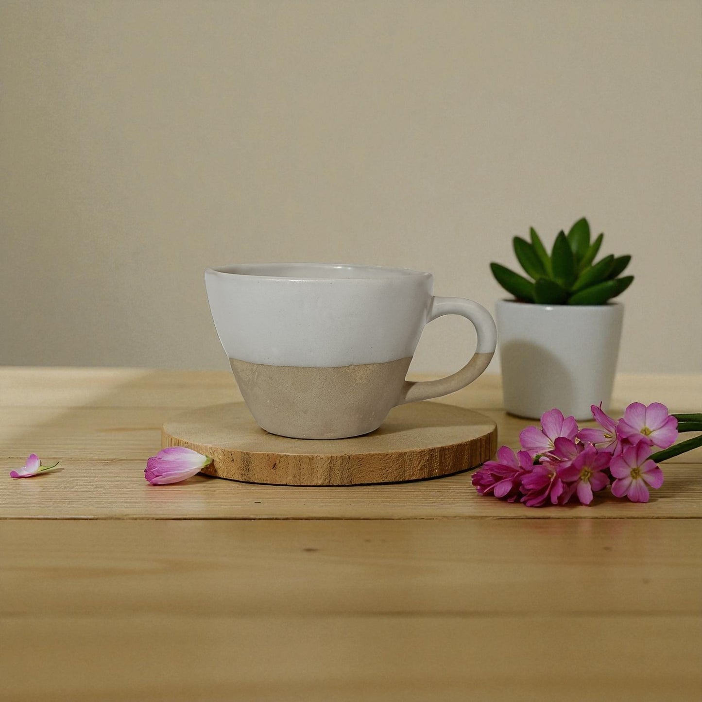 Ceramic mug with a wooden coaster on a wooden surface with flowers and a small plant.
