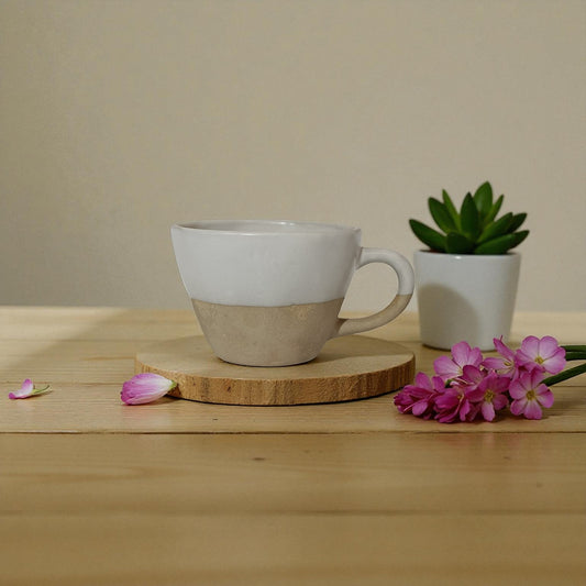 Ceramic mug with a wooden coaster on a wooden surface with flowers and a small plant.
