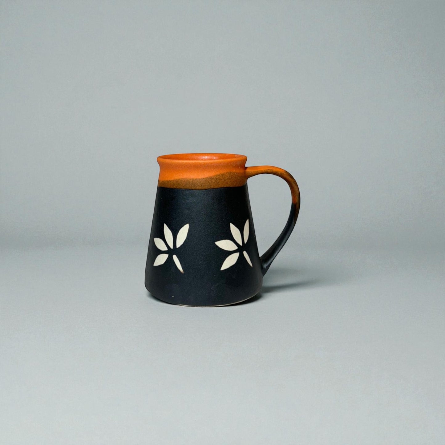 Ceramic mug with black body, orange rim, and white floral patterns on a gray background
