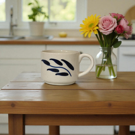 Ceramic mug with blue leaf design on a wooden table in a kitchen setting.