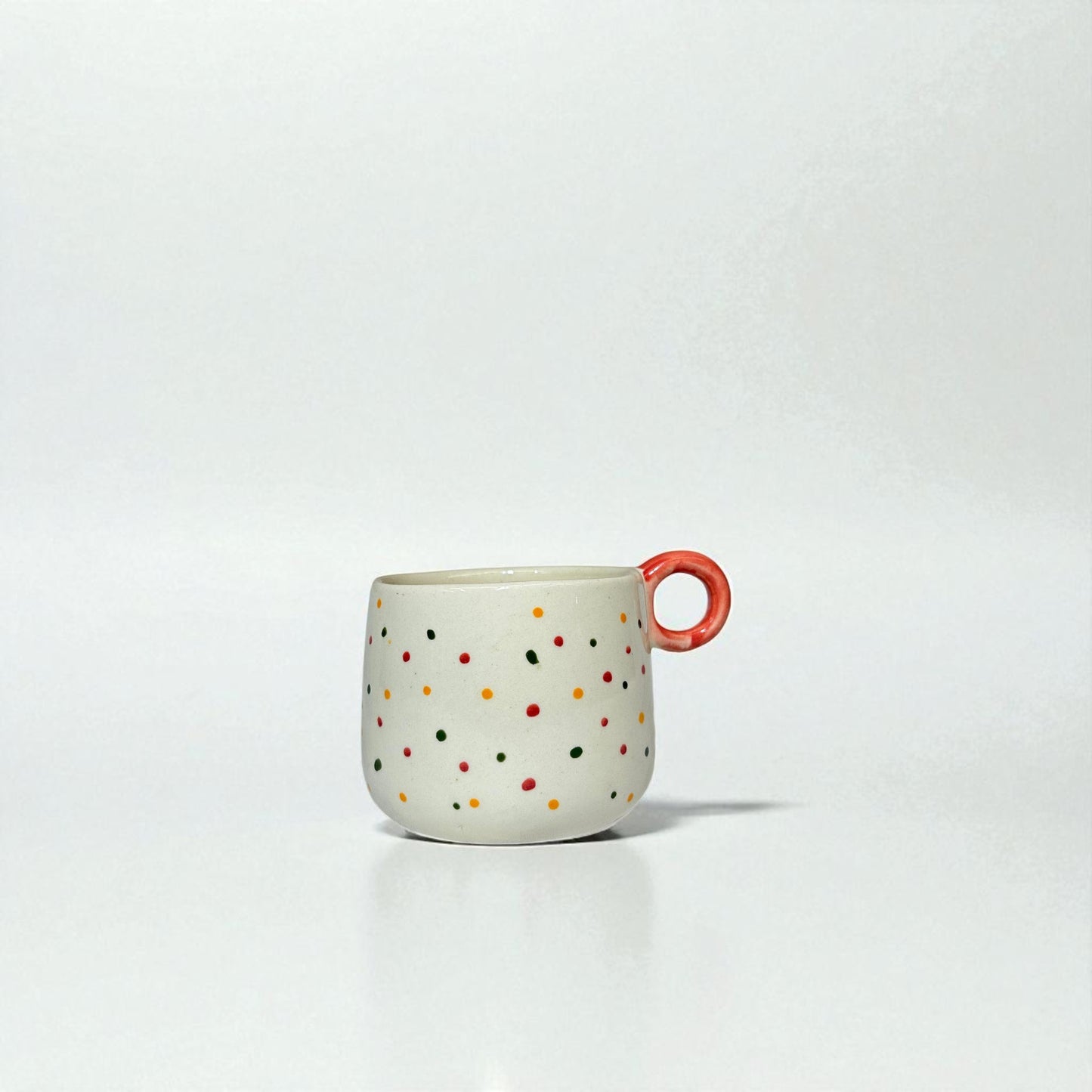 Ceramic mug with colorful polka dots and a red handle on a white background