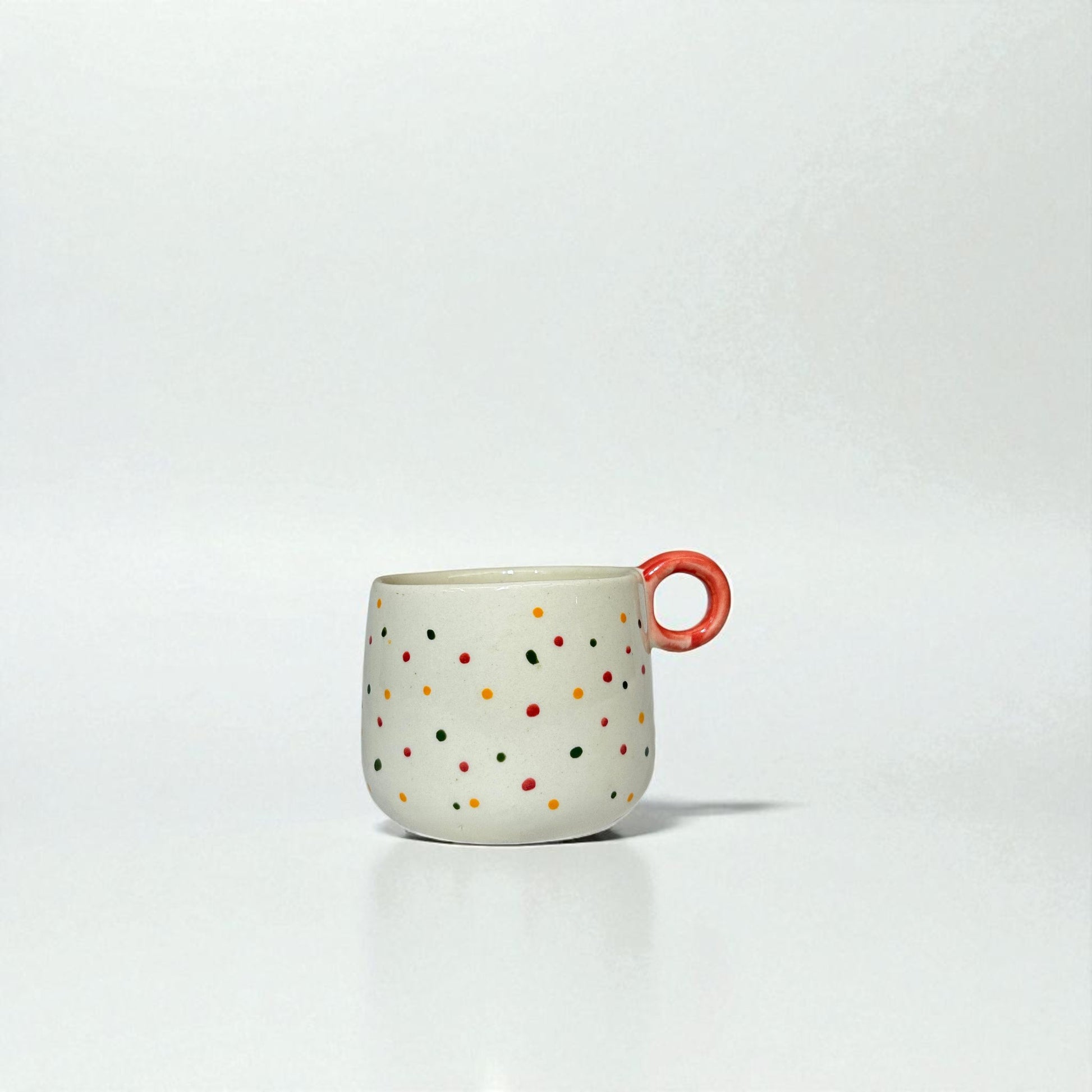 Ceramic mug with colorful polka dots and a red handle on a white background