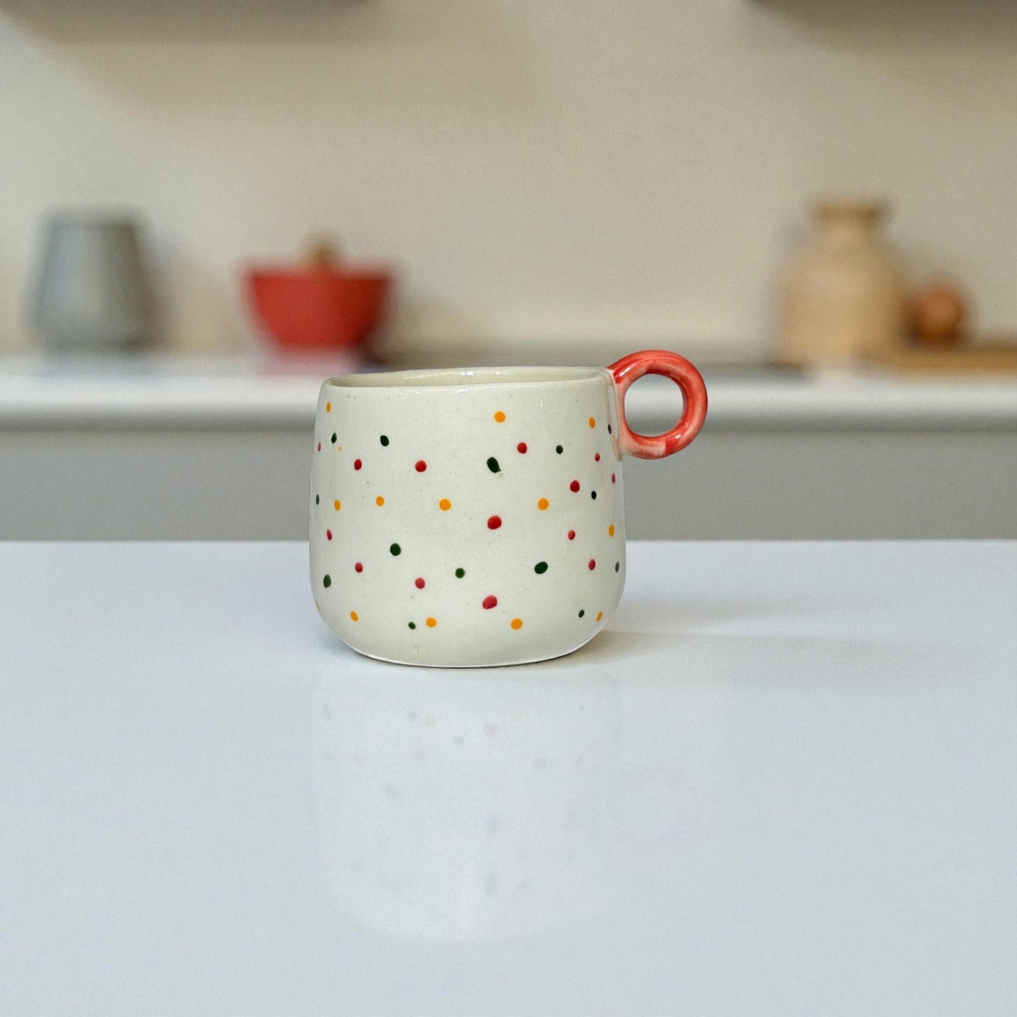 Ceramic mug with colorful polka dots and a red handle on a white surface.