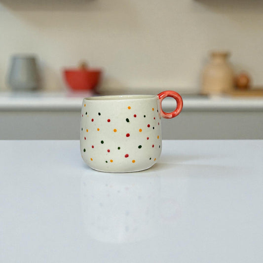 Ceramic mug with colorful polka dots and a red handle on a white surface.