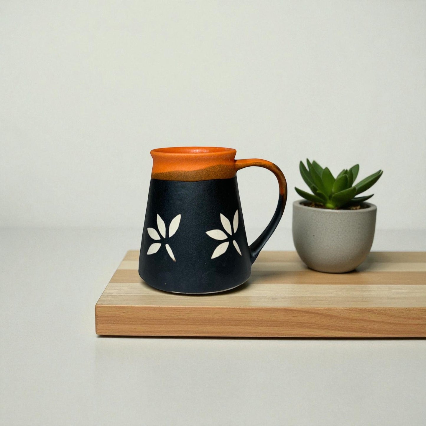 Ceramic mug with floral design on a wooden surface next to a potted plant.