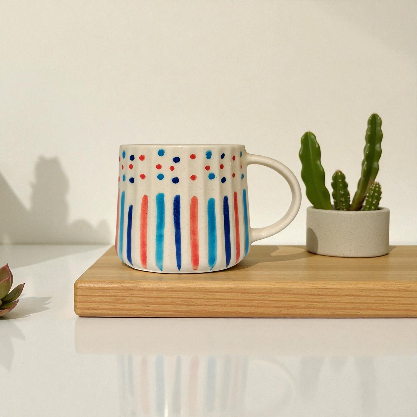 Colorful mug with polka dot and stripe design on a wooden surface with a plant in the background