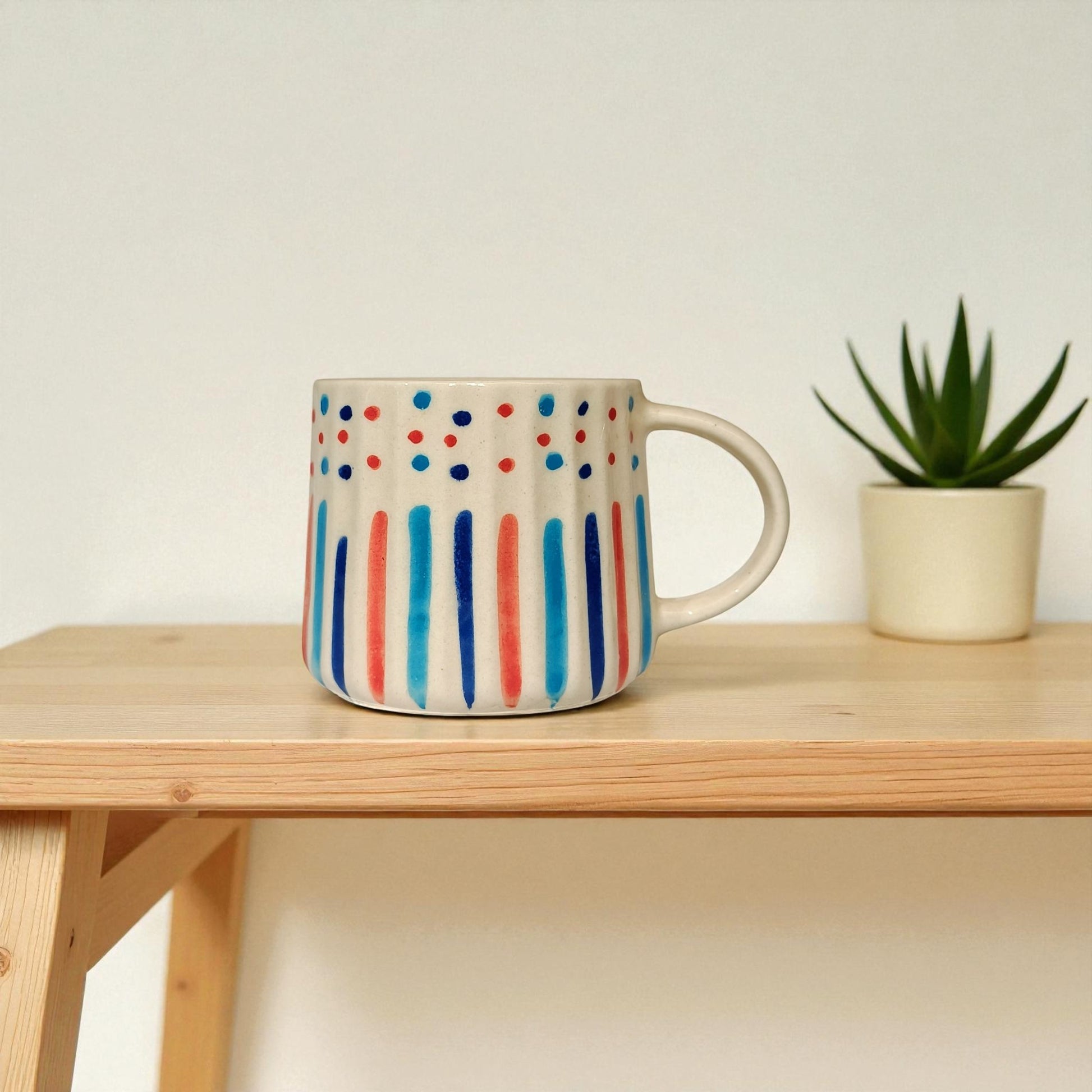 Colorful mug with polka dot and stripe pattern on a wooden surface with a plant in the background