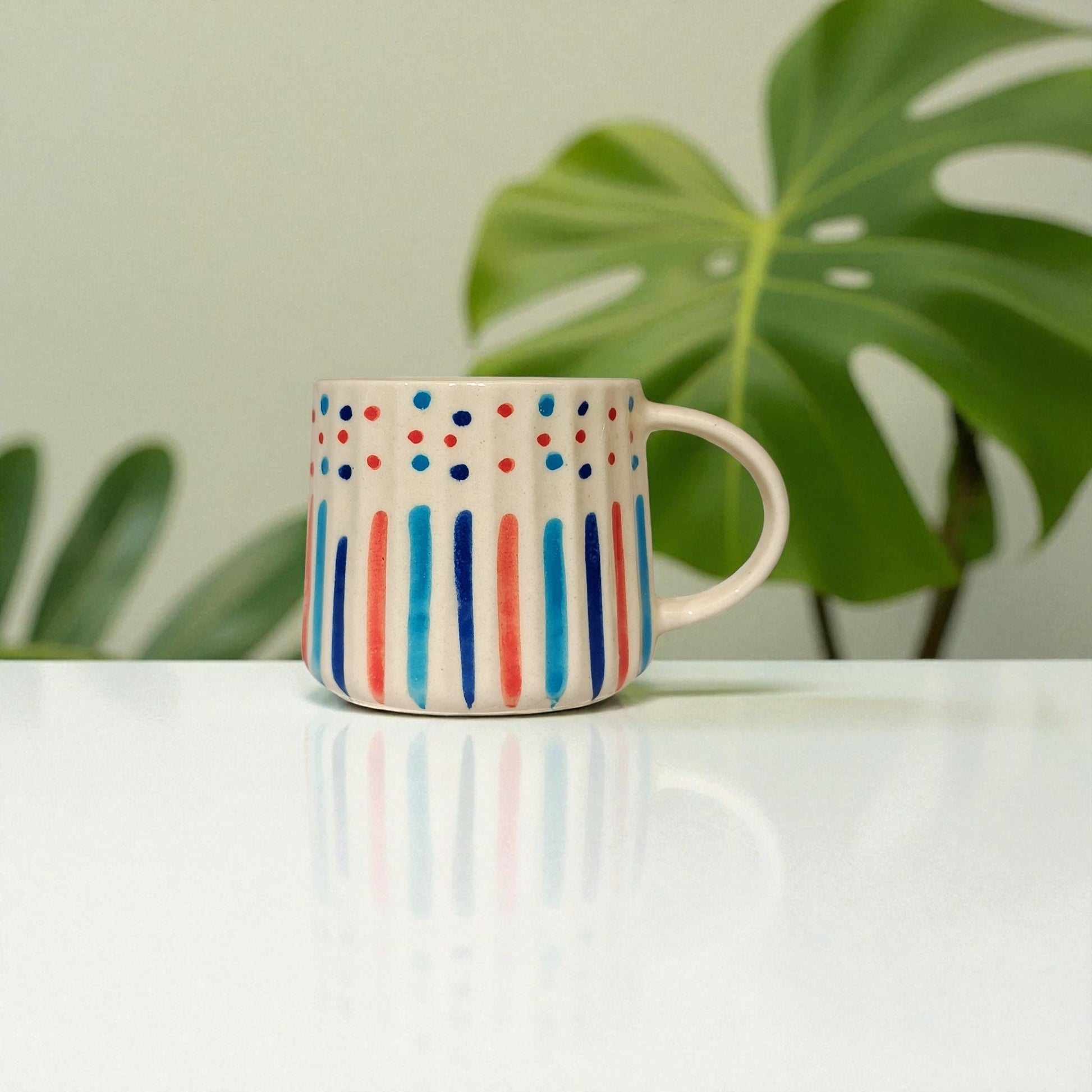 Colorful polka dot mug on a white surface with green leaves in the background