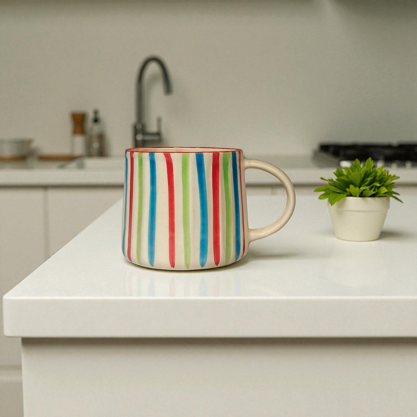 Colorful striped mug on a kitchen counter with a plant and sink in the background