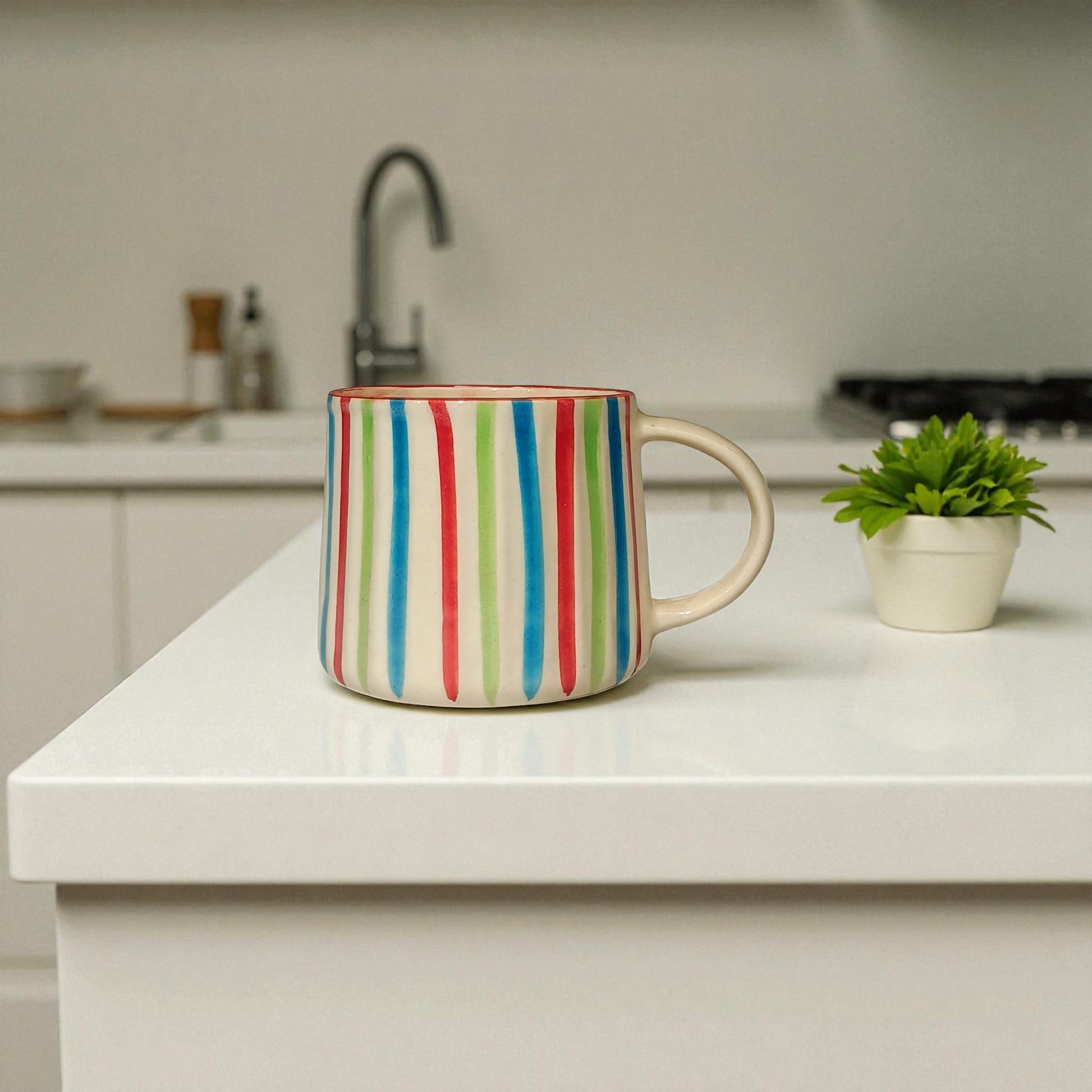 Colorful striped mug on a kitchen counter with a plant and sink in the background