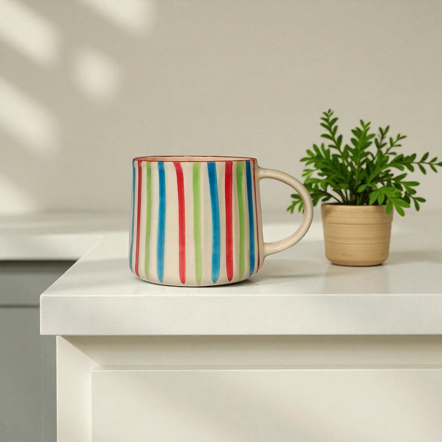 Colorful striped mug on a white surface with a plant in the background