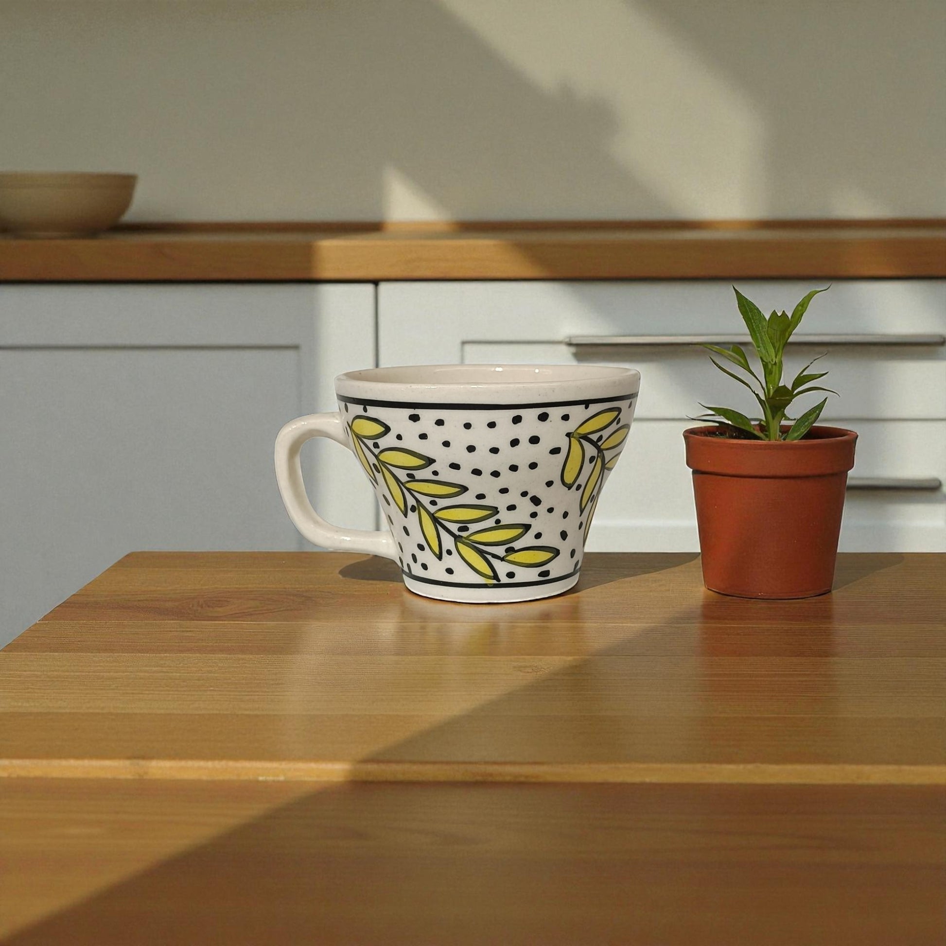 Decorative mug with yellow leaf pattern on a wooden surface next to a potted plant