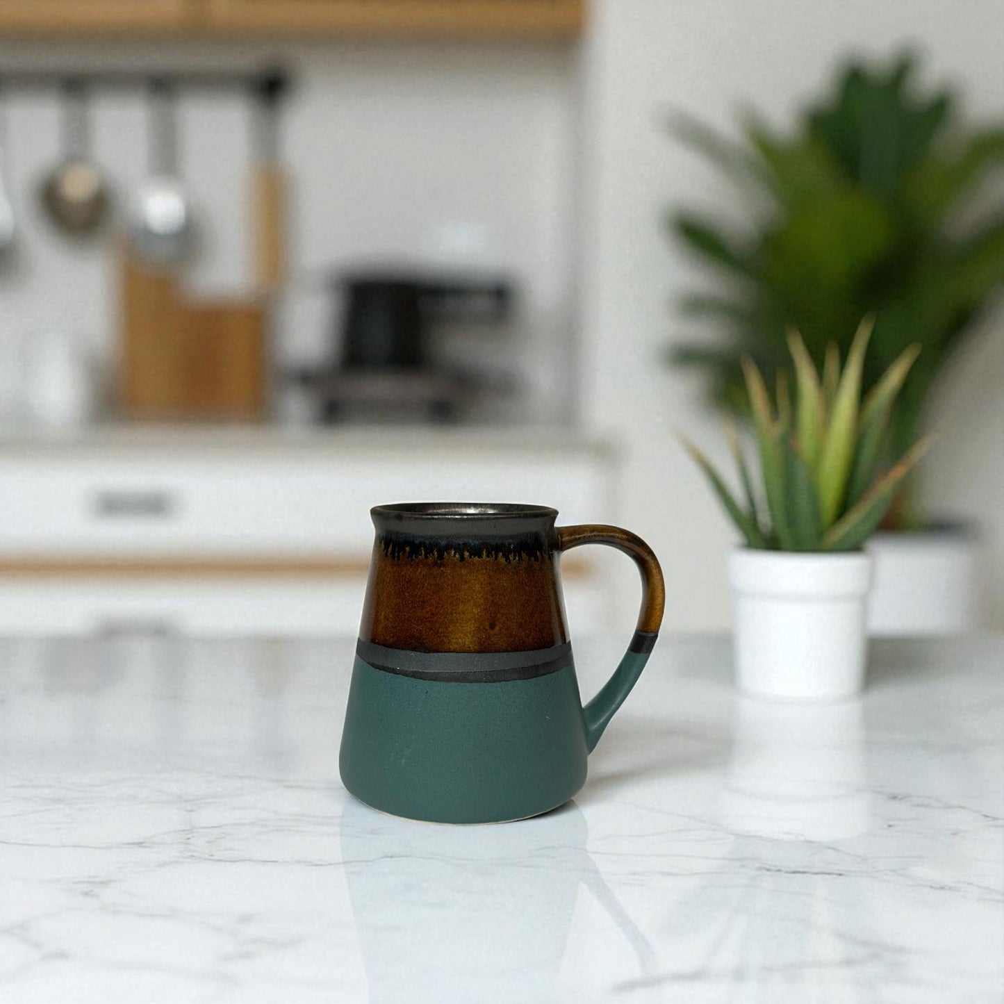 Green and brown ceramic mug on a kitchen counter with blurred background