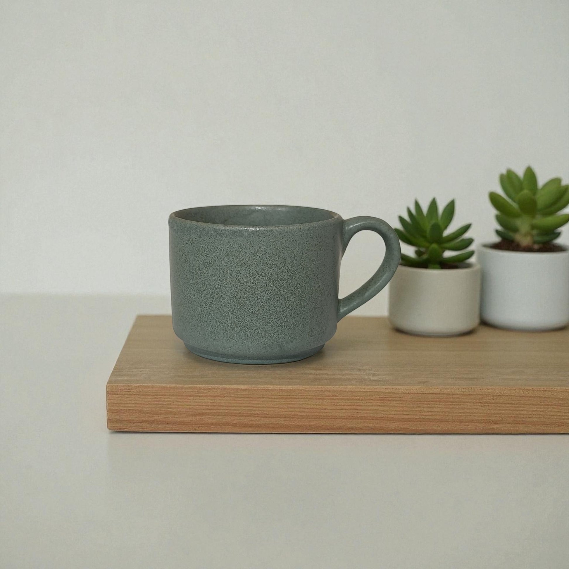 Green ceramic mug on a wooden surface with two small plants in the background