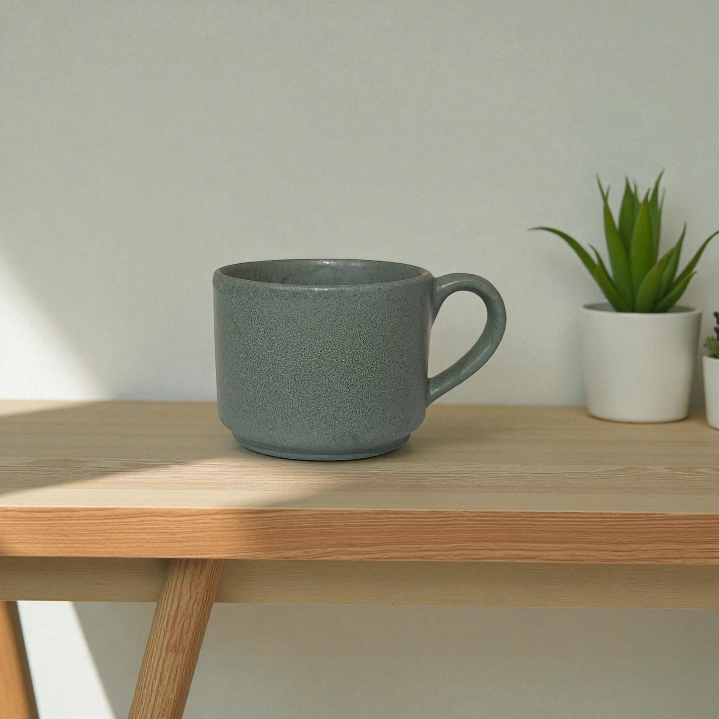 Green mug on a wooden table with a plant in the background