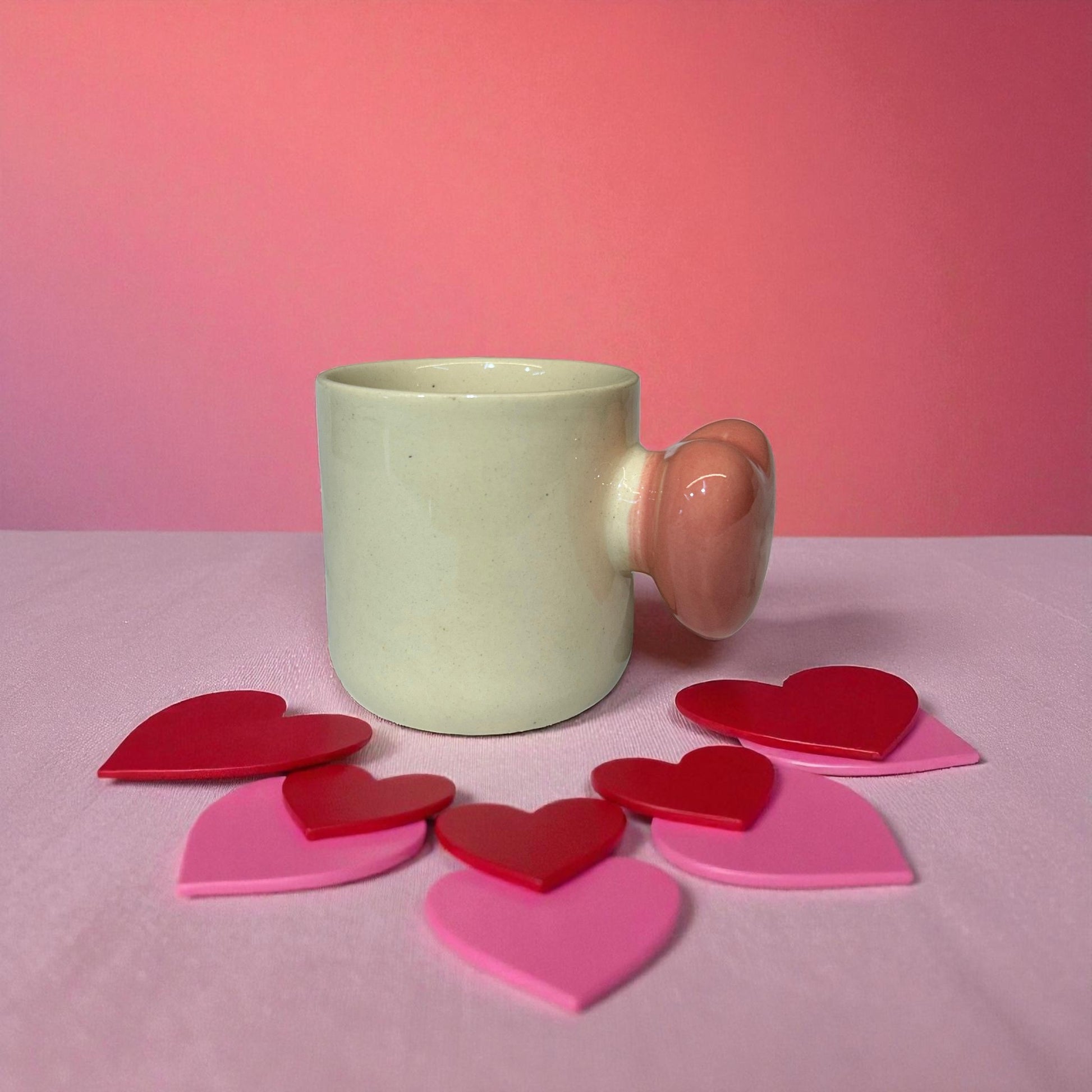 Green mug with pink handle on a pink surface with heart-shaped objects