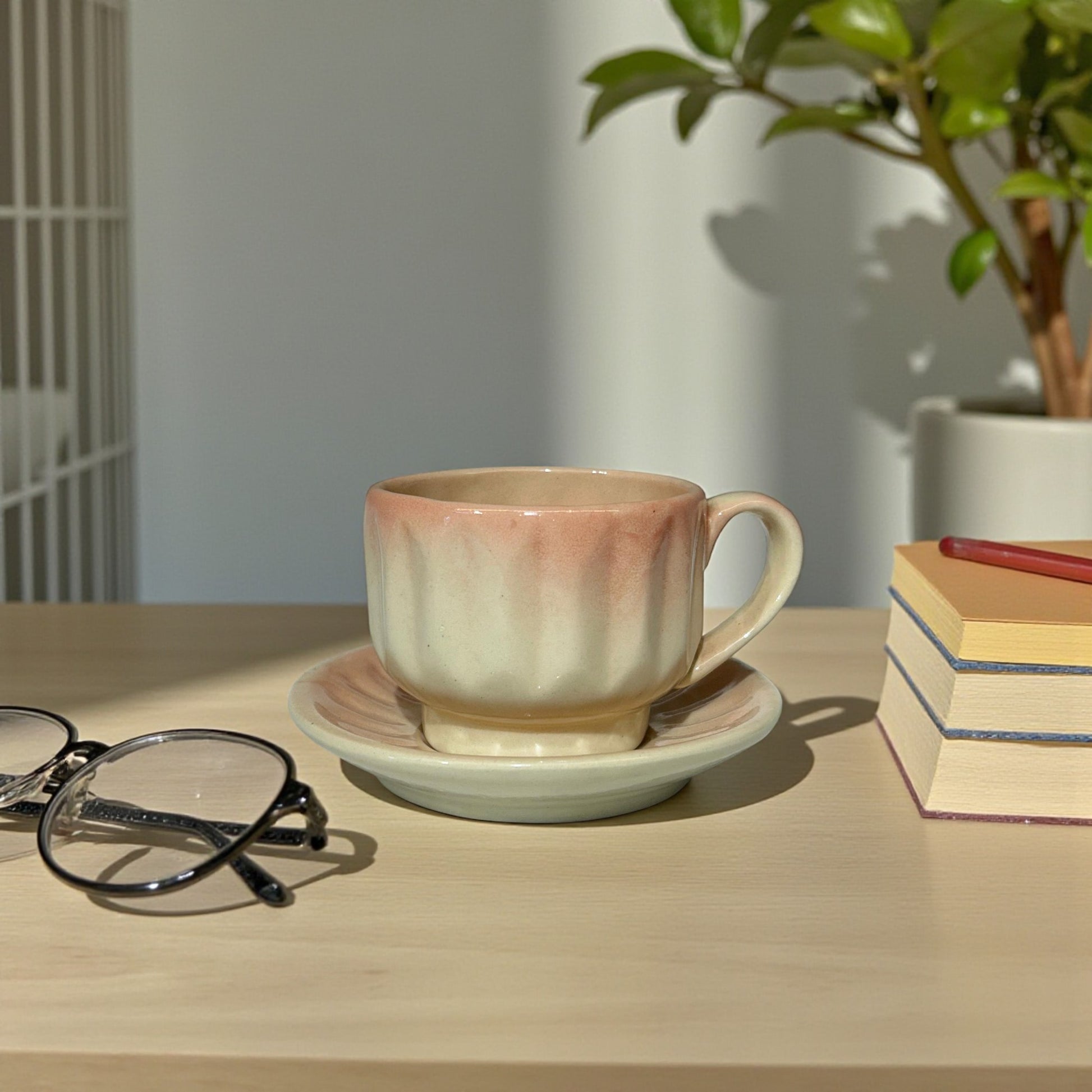 Ceramic cup and saucer on a wooden table with glasses and books in the background