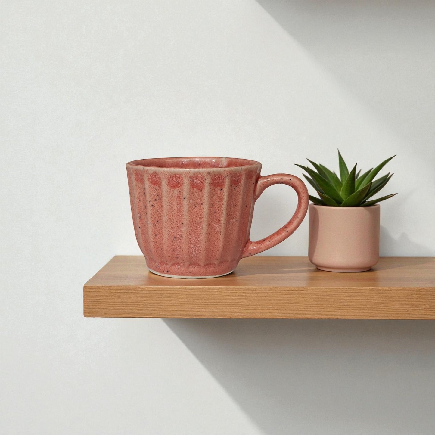 Pink mug and small plant on a wooden shelf against a white wall