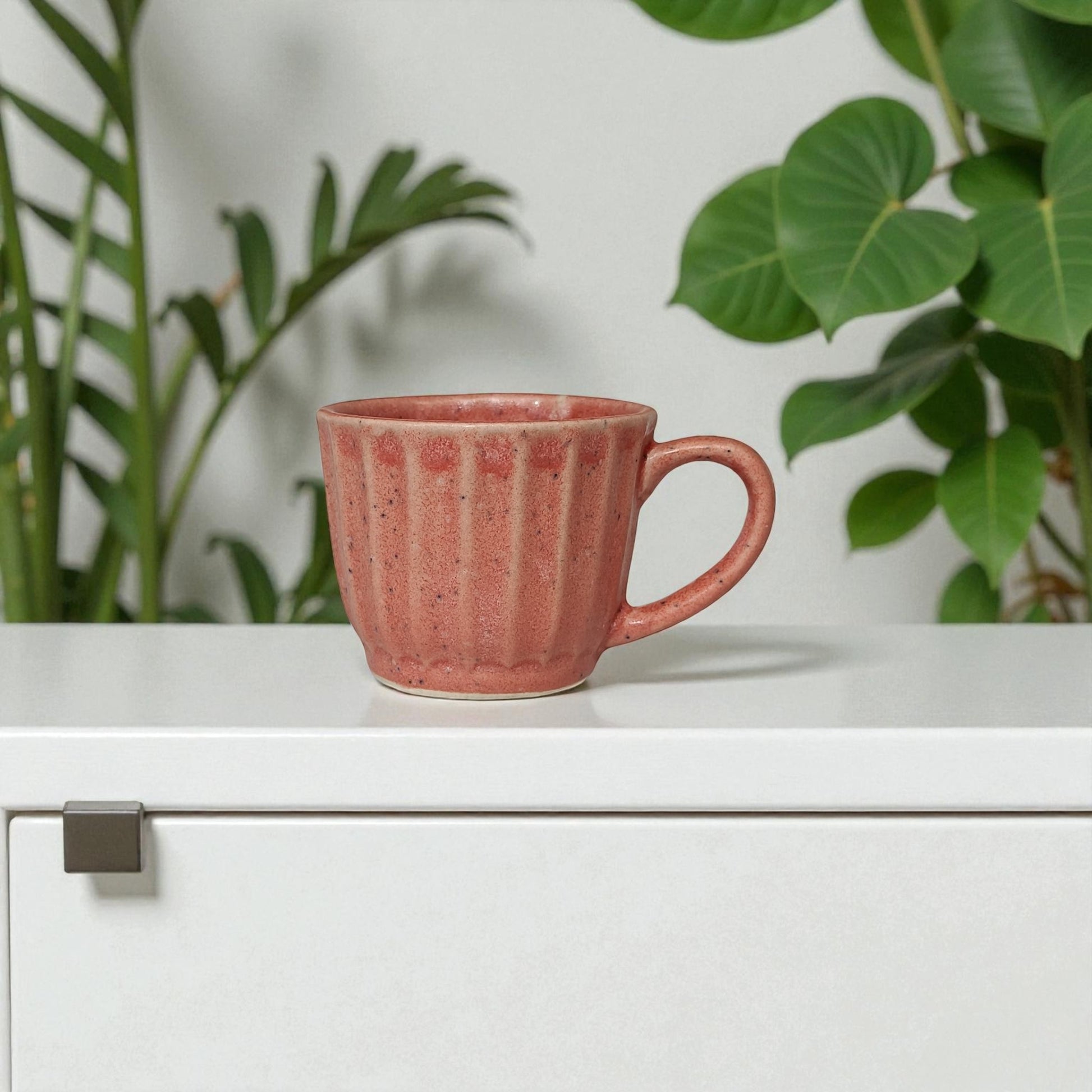 Pink mug on a white surface with green plants in the background